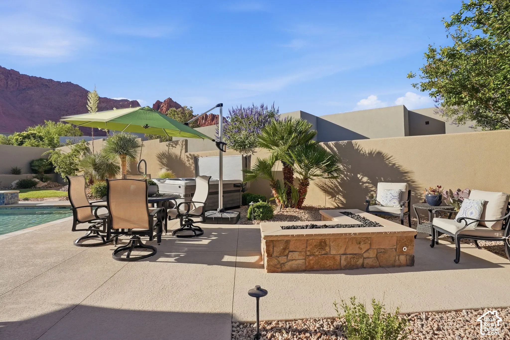Expansive patio featuring a built-in stone fire pit, adjacent pool, and surrounding desert landscaping
