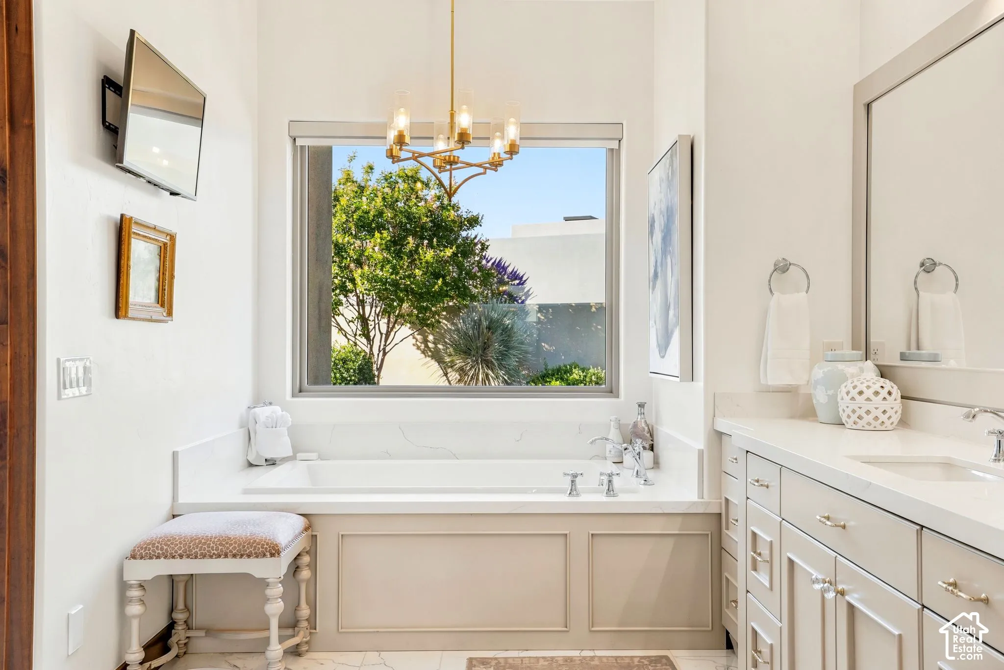 Built-in soaking tub with a surrounding stone-finish deck, an overhead gold-tone chandelier, and a double vanity with an integrated sink and stone-finish countertop