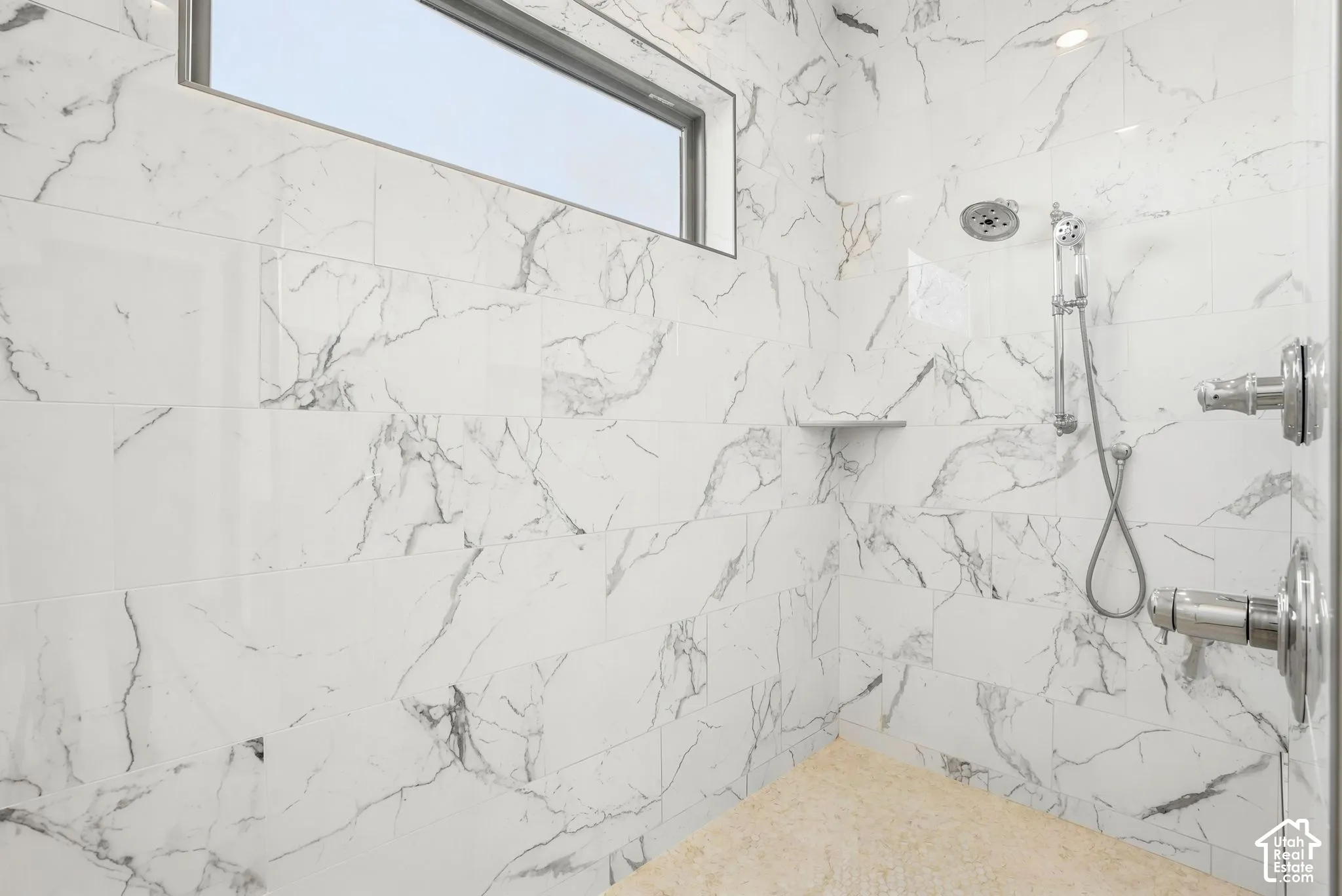Spacious shower with large format white tile, a built-in shower bench, overhead shower head, and a handheld shower wand