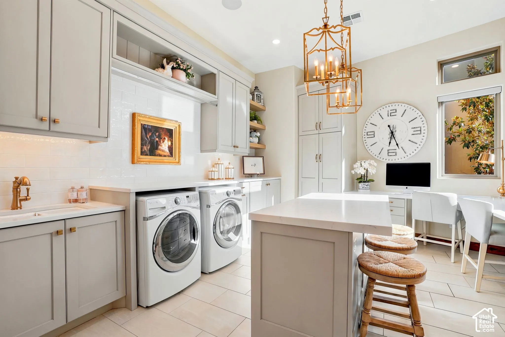 Light-toned cabinetry with brass hardware, integrated washer and dryer units, white subway tile backsplash, white countertop island, and tiled flooring