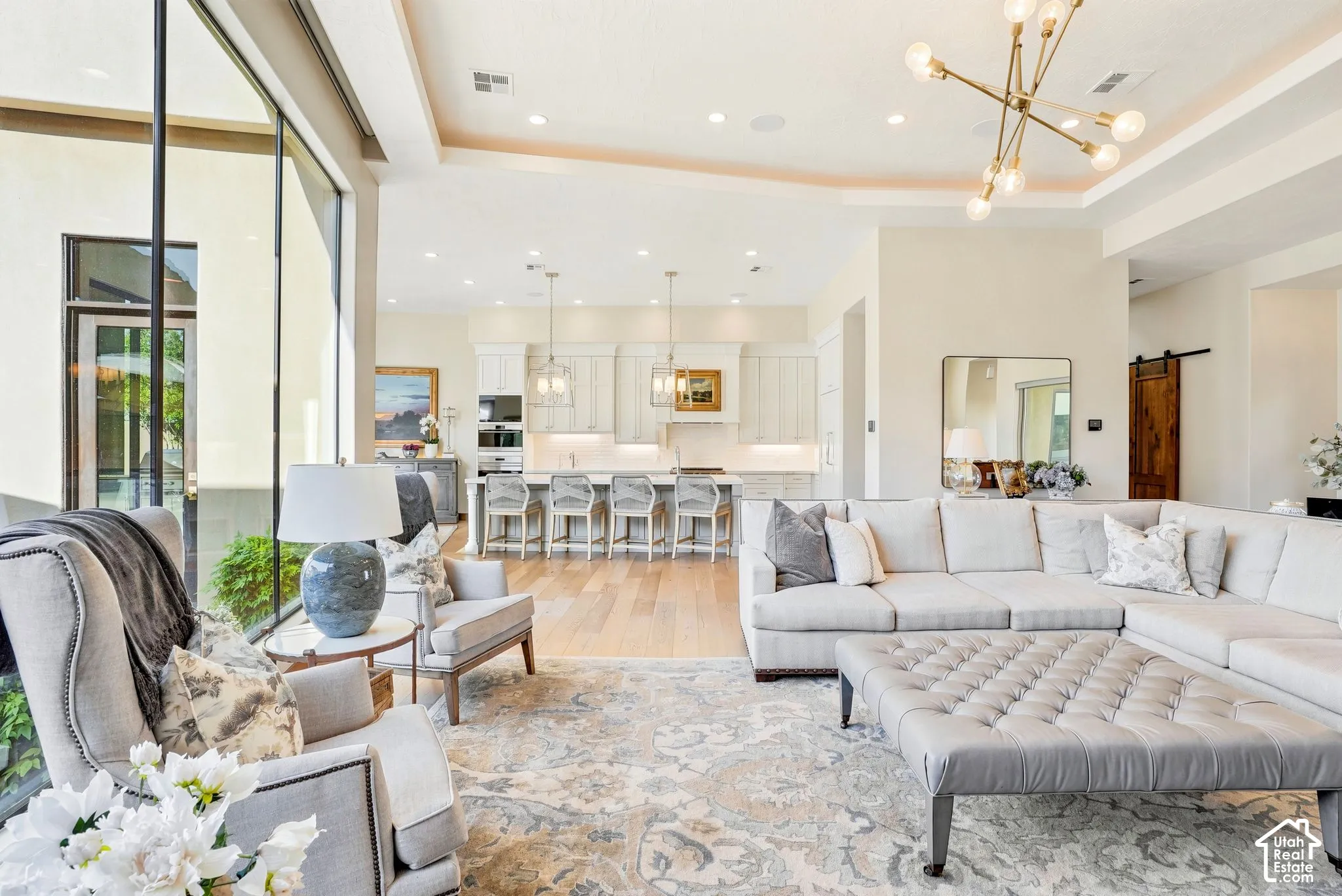 Expansive open-concept living area featuring high ceilings, large windows, wood-finish flooring, and a modern chandelier