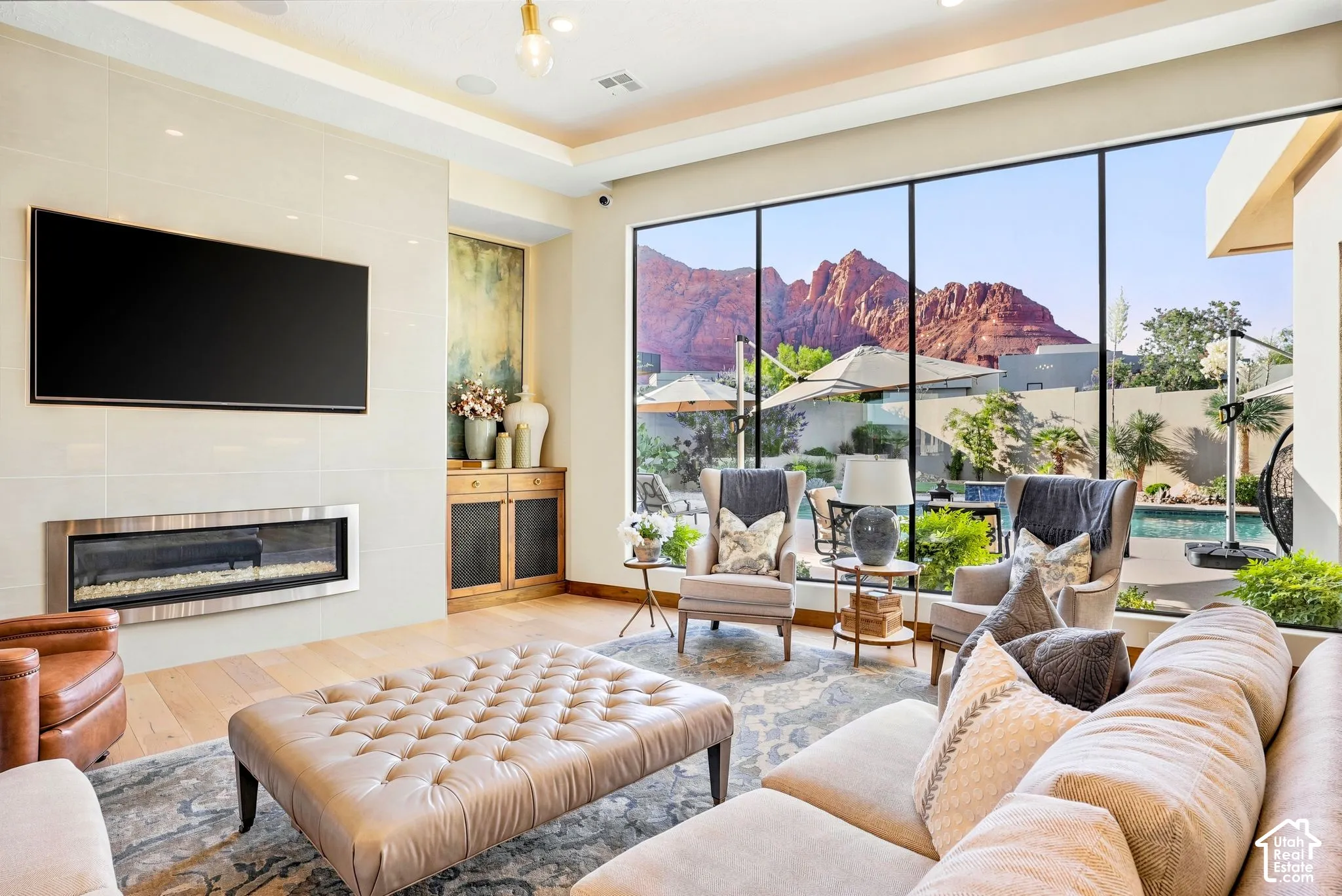 Expansive floor-to-ceiling windows, modern linear fireplace, wood-finish flooring, recessed lighting, and a built-in wood-front cabinet
