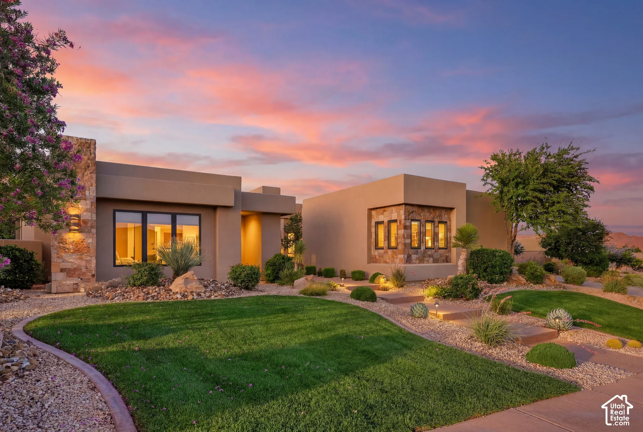 Modern exterior with stucco finish and stone accents, featuring a manicured lawn, xeriscaped landscaping, and exterior wall sconces