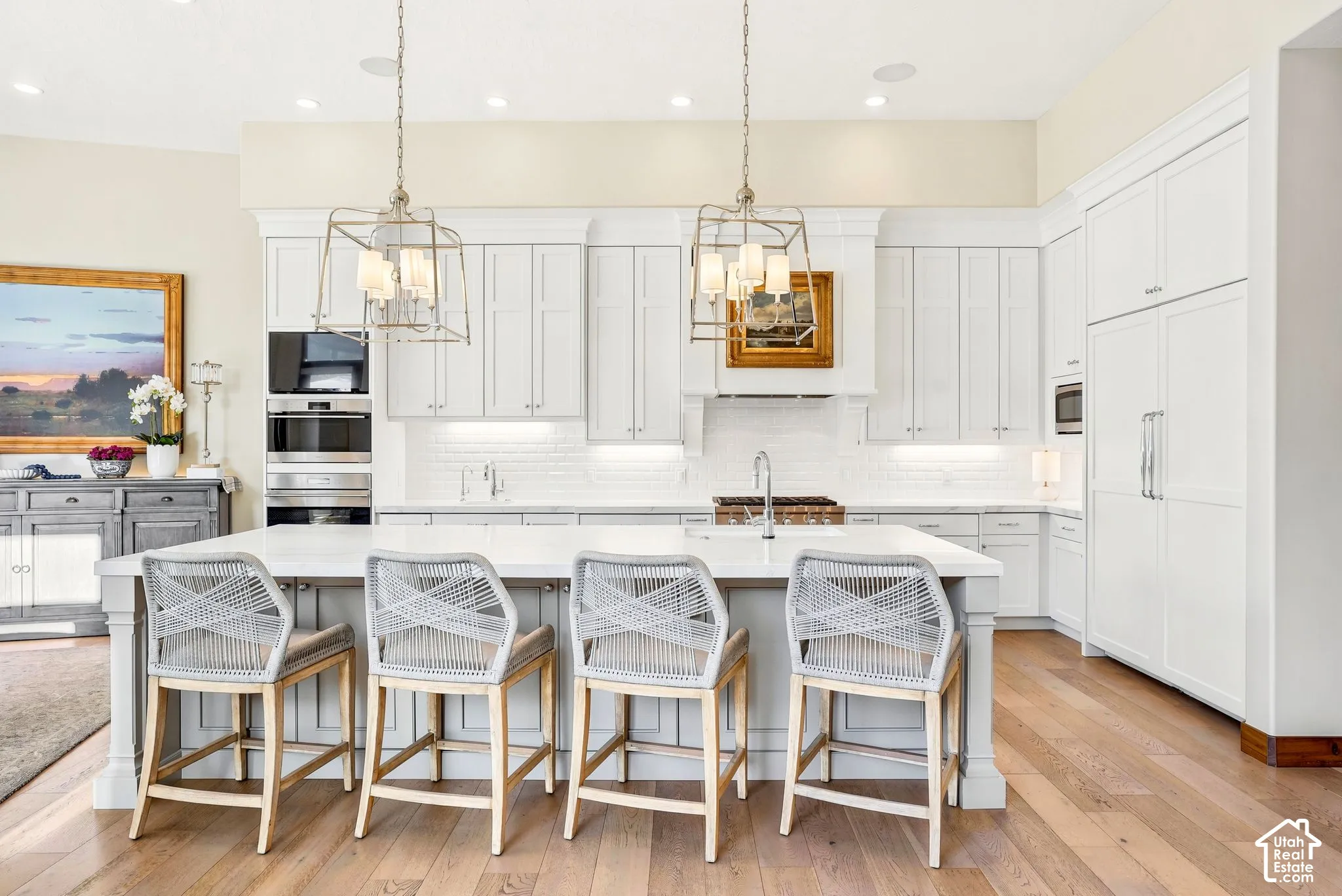 Kitchen featuring white cabinetry, wood-finish flooring, two large pendant lights, an integrated refrigerator, and a kitchen island with seating