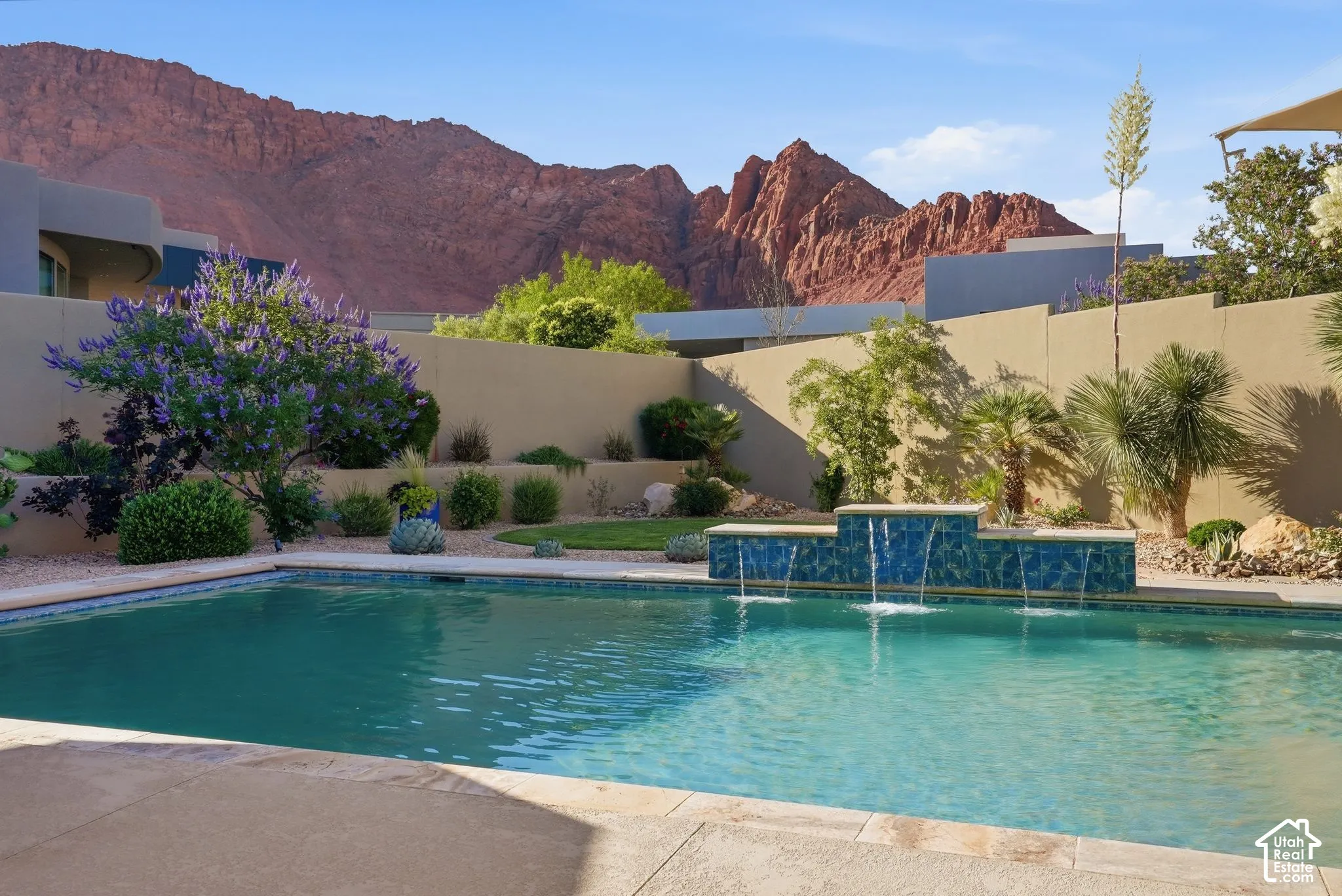 Swimming pool with integrated tiled water feature, bordered by a concrete patio and a landscaped privacy wall, all set against a prominent red rock mountain backdrop