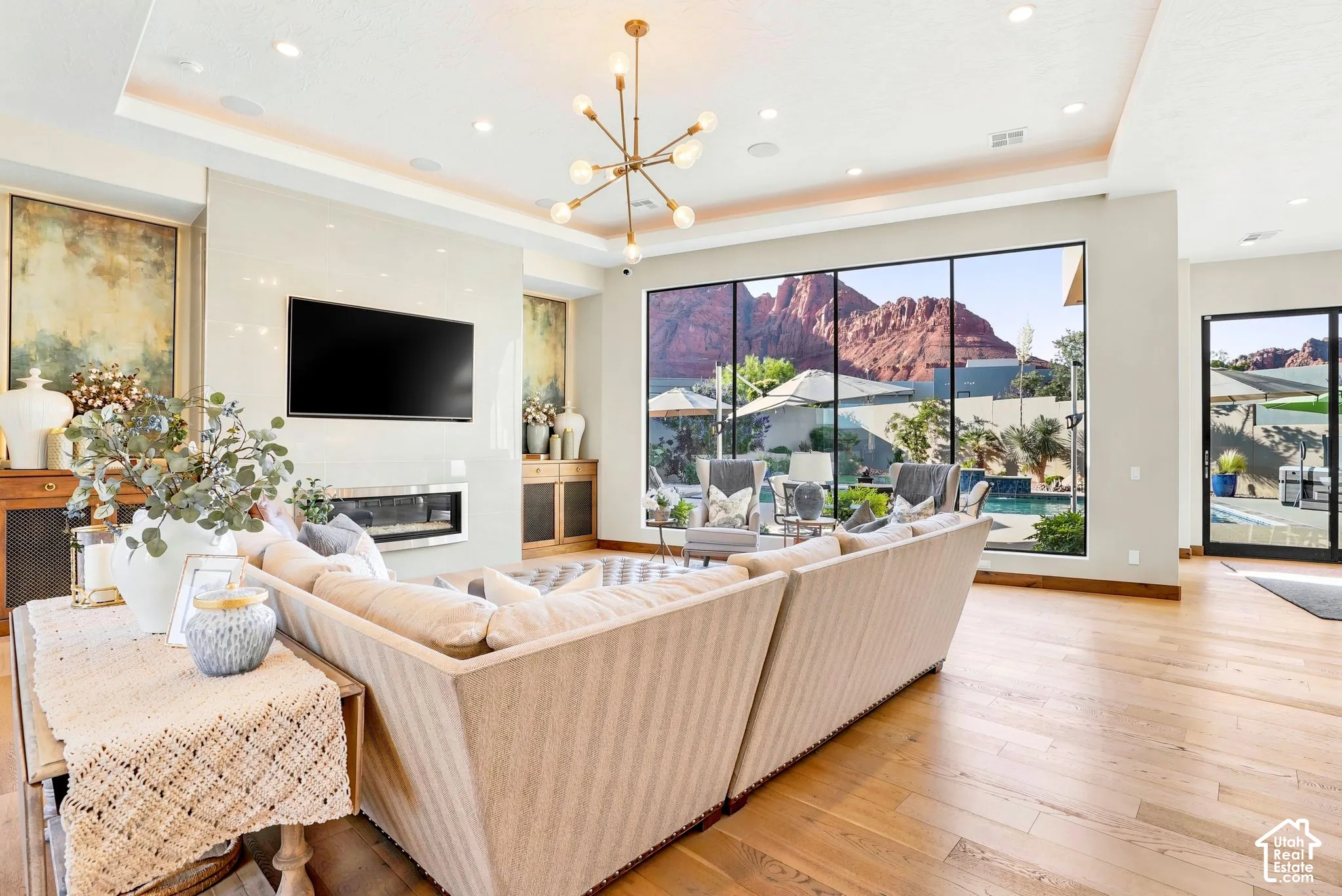 Expansive floor-to-ceiling windows, wood-finish flooring, a contemporary fireplace, and a decorative ceiling light fixture