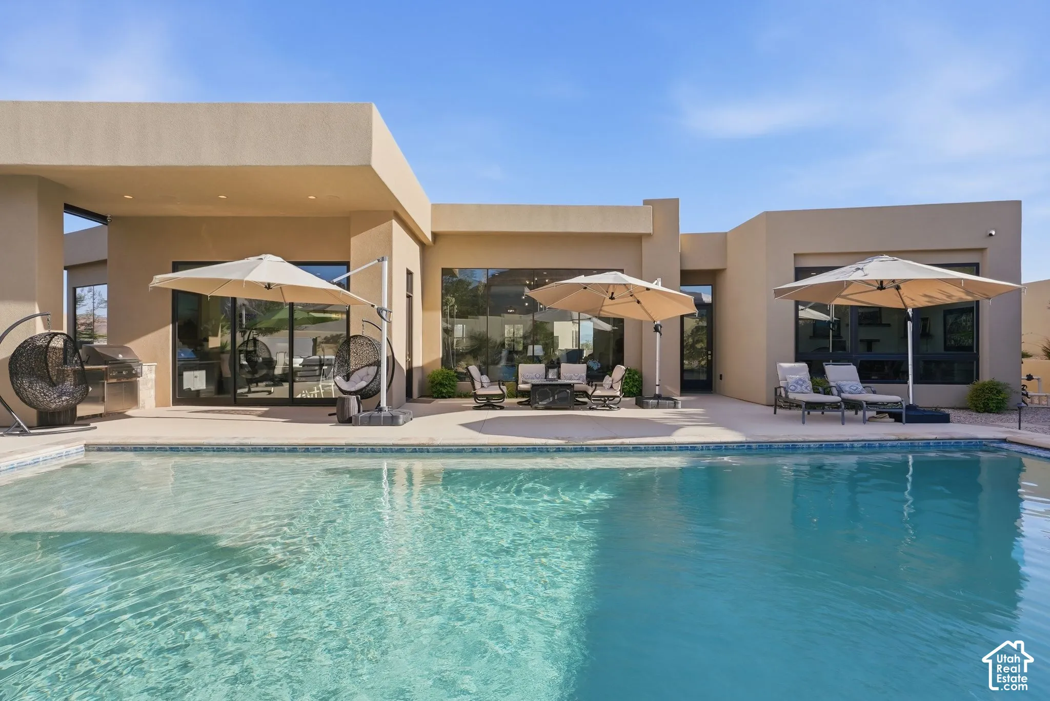Pool with a tiled edge, an expansive patio, an outdoor kitchen with a built-in grill, and multiple floor-to-ceiling glass doors