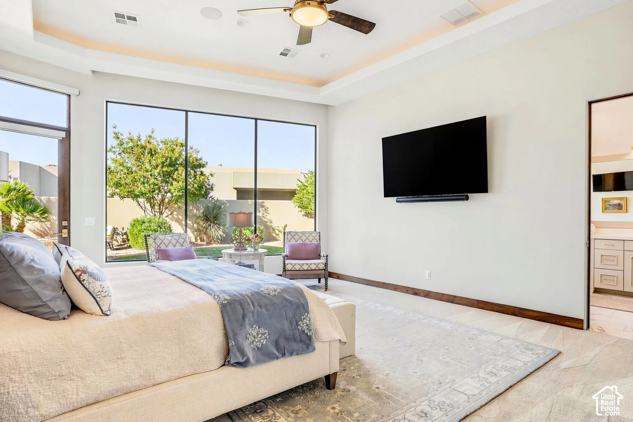 Recessed ceiling with perimeter lighting, large format window, ceiling fan, wood-finish flooring, and a wall-mounted television
