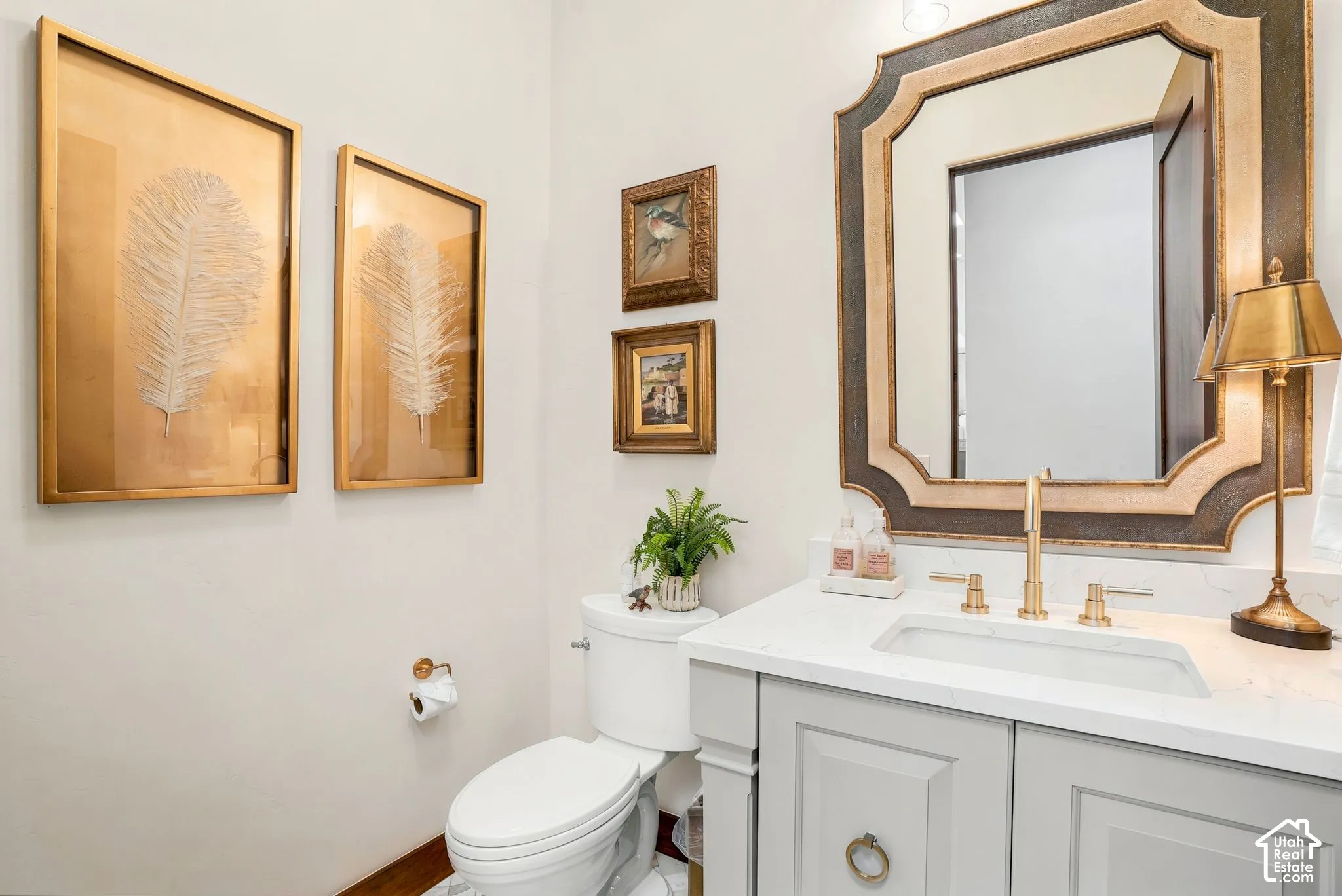 White vanity with a rectangular undermount sink, brass-finish faucet, and white countertop