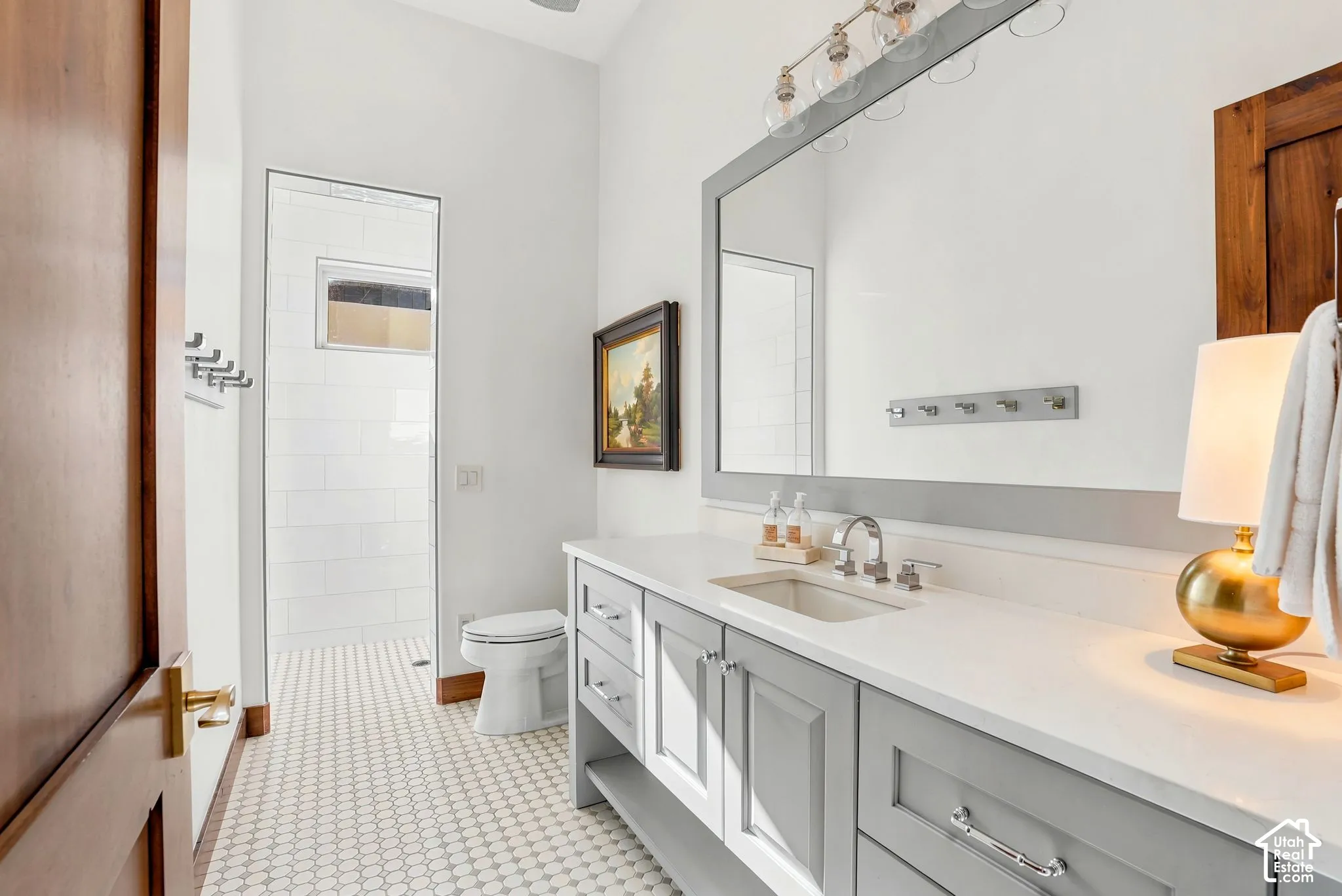 White hexagonal tile flooring, gray vanity with chrome hardware, integrated sink with chrome faucet, large framed mirror, and a walk-in shower with subway tile