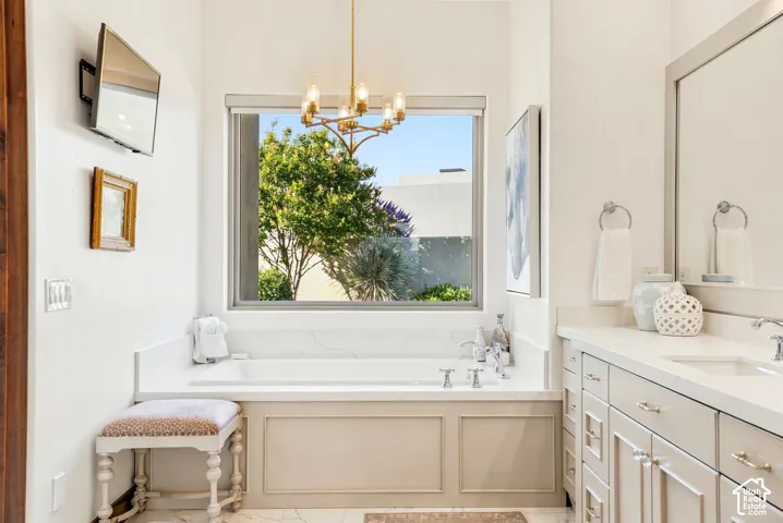 Built-in soaking tub with a surrounding stone-finish deck, an overhead gold-tone chandelier, and a double vanity with an integrated sink and stone-finish countertop