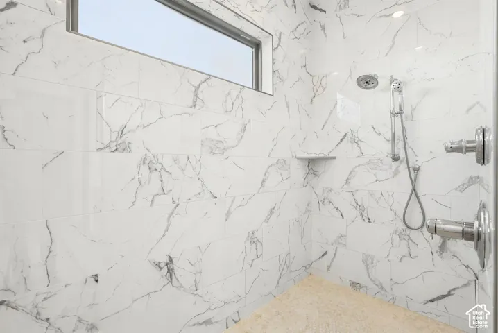 Spacious shower with large format white tile, a built-in shower bench, overhead shower head, and a handheld shower wand