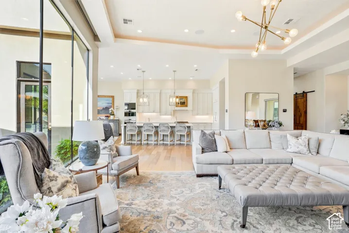 Expansive open-concept living area featuring high ceilings, large windows, wood-finish flooring, and a modern chandelier