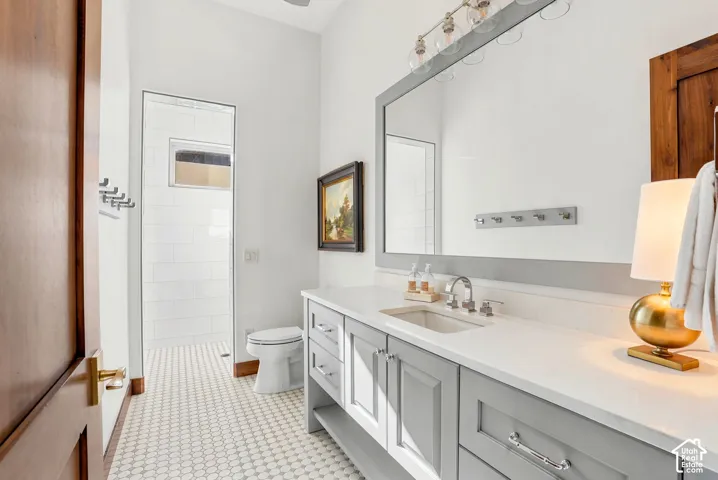 White hexagonal tile flooring, gray vanity with chrome hardware, integrated sink with chrome faucet, large framed mirror, and a walk-in shower with subway tile