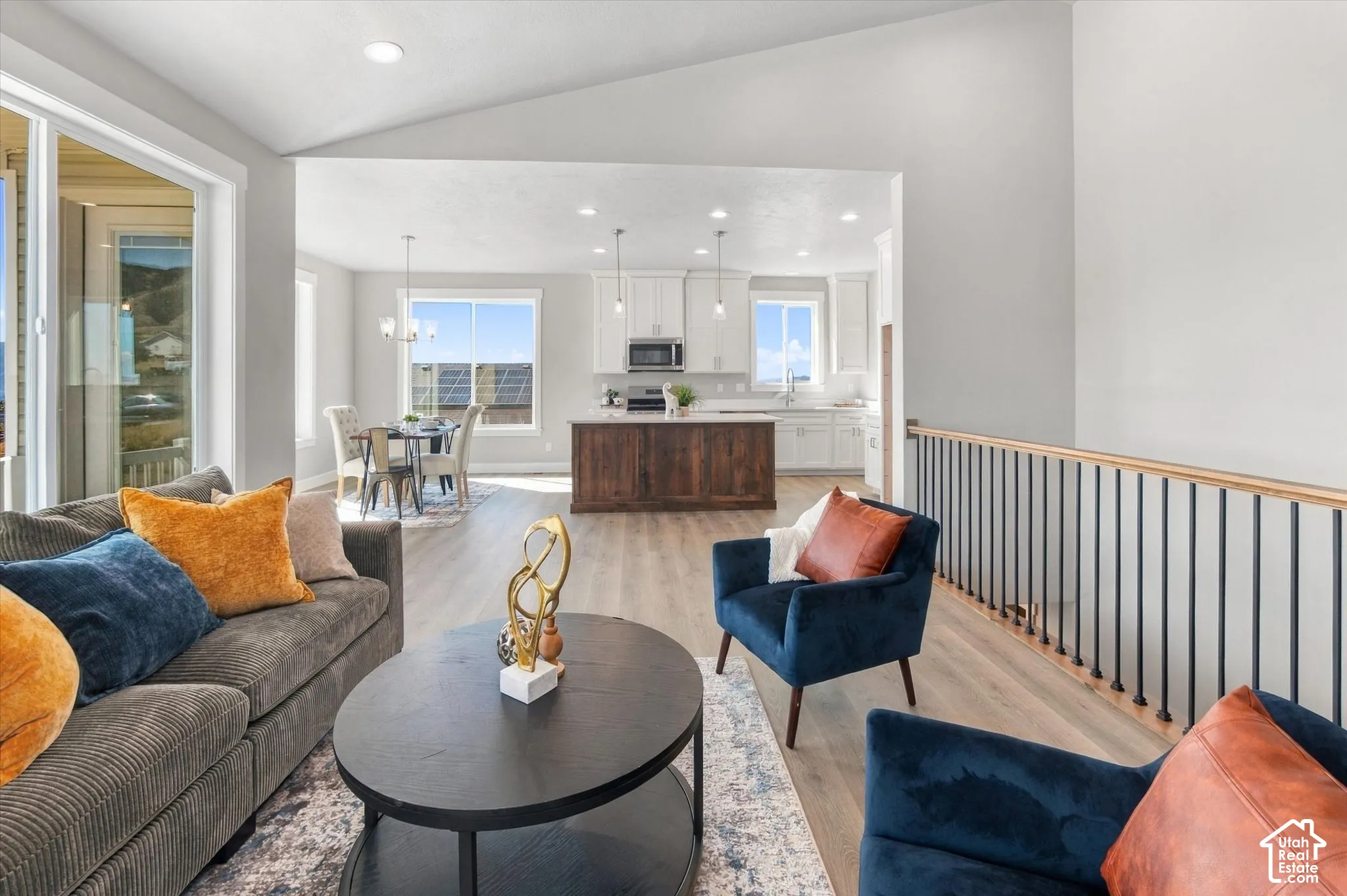 Open-concept living area with vaulted ceilings, wood-finish flooring, and a contemporary railing
