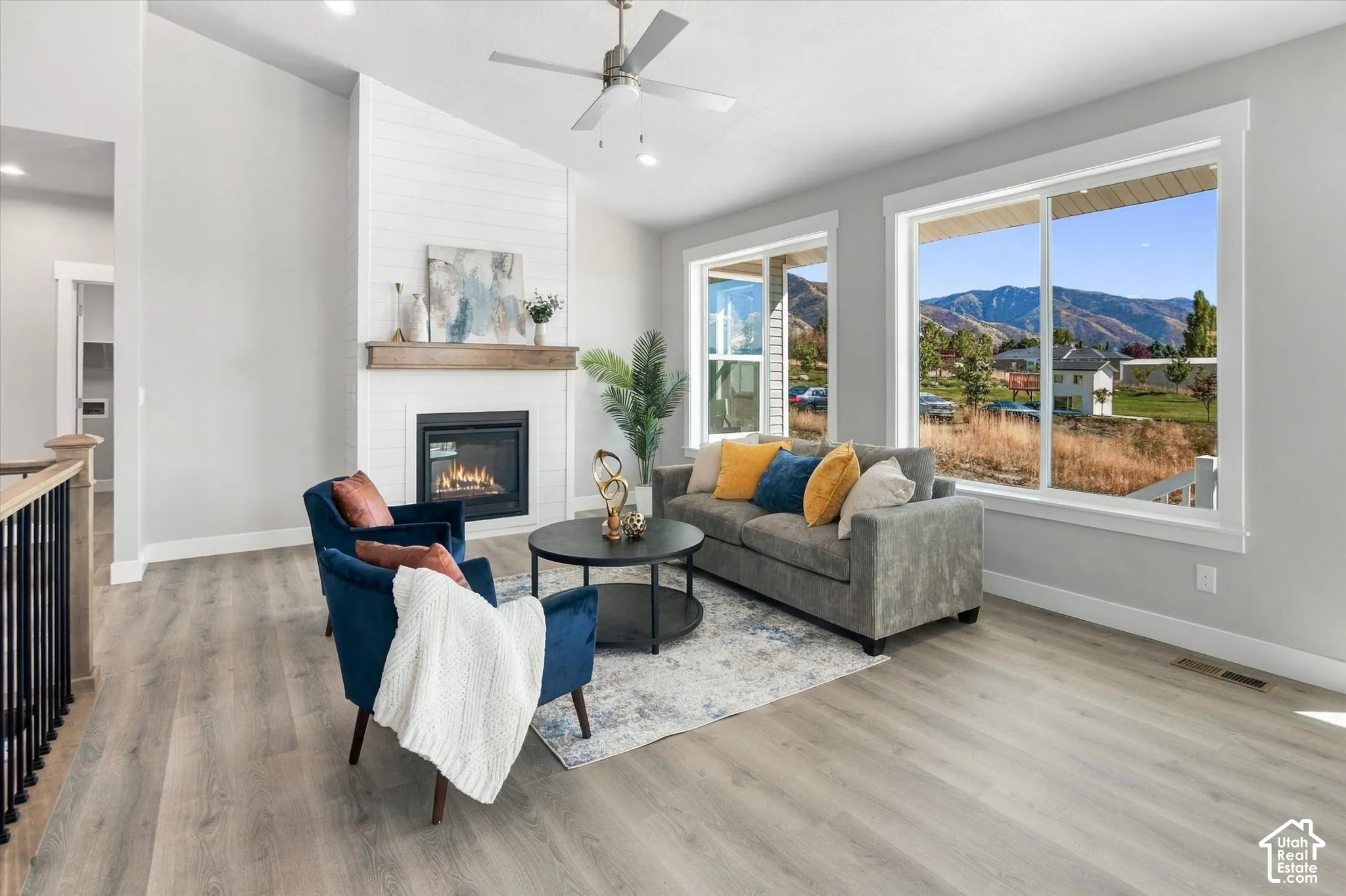 Vaulted ceiling with a ceiling fan, fireplace with a wood mantle, wood-finish flooring, and large windows with mountain scenery