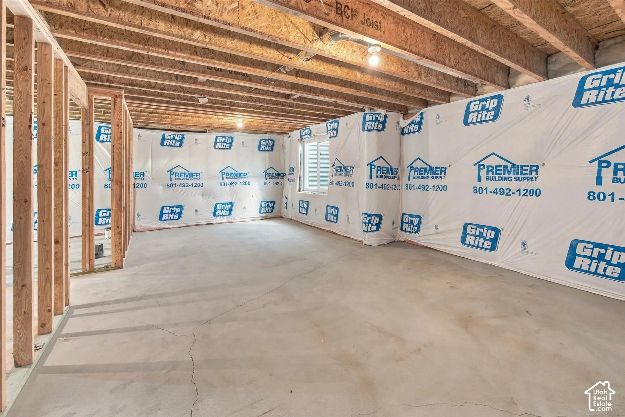 Framed interior walls, exposed ceiling joists, concrete flooring, and a single window with horizontal blinds