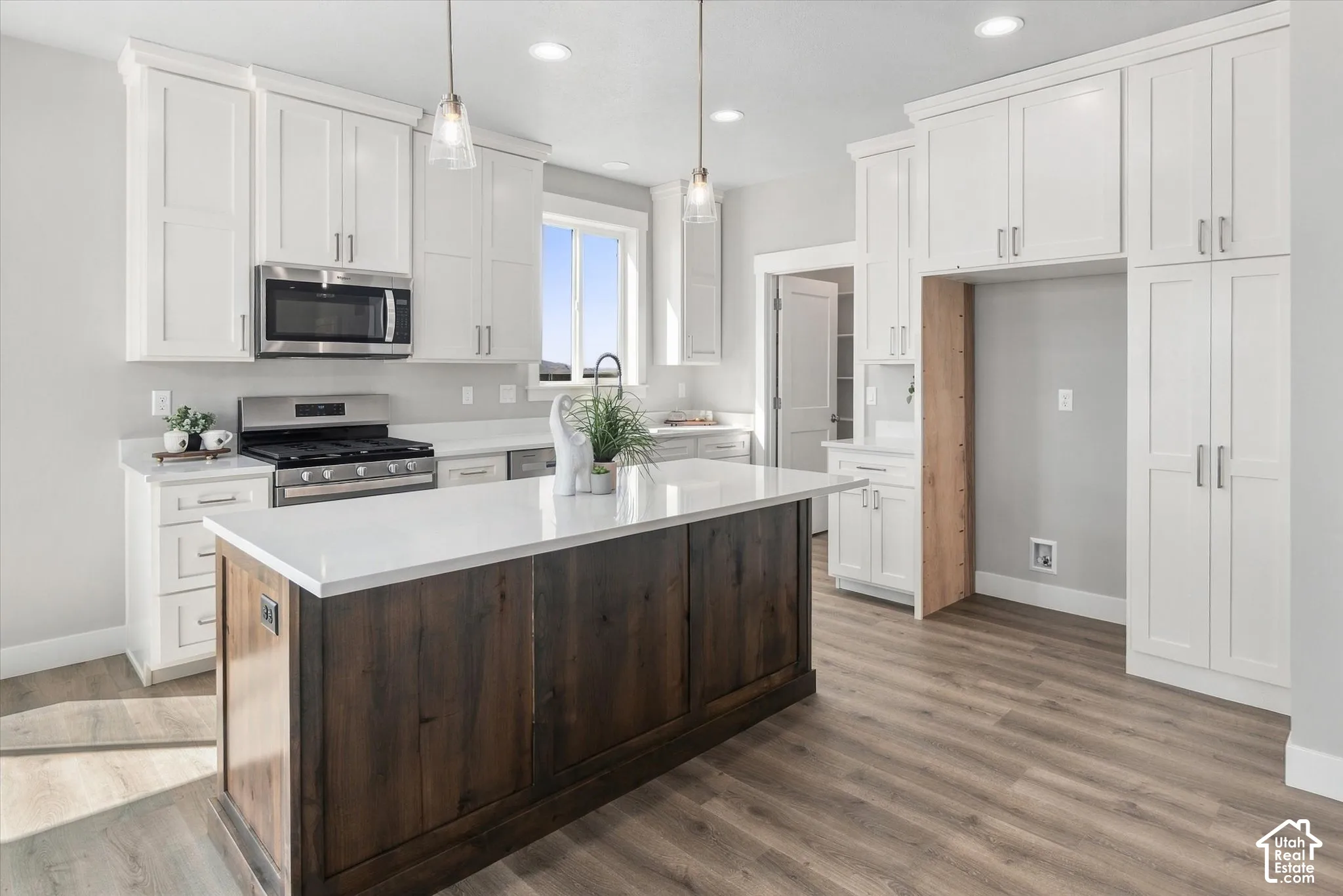 Spacious kitchen featuring white shaker cabinetry, stainless steel appliances, a large center island with a wood-finish base, and light wood-finish flooring