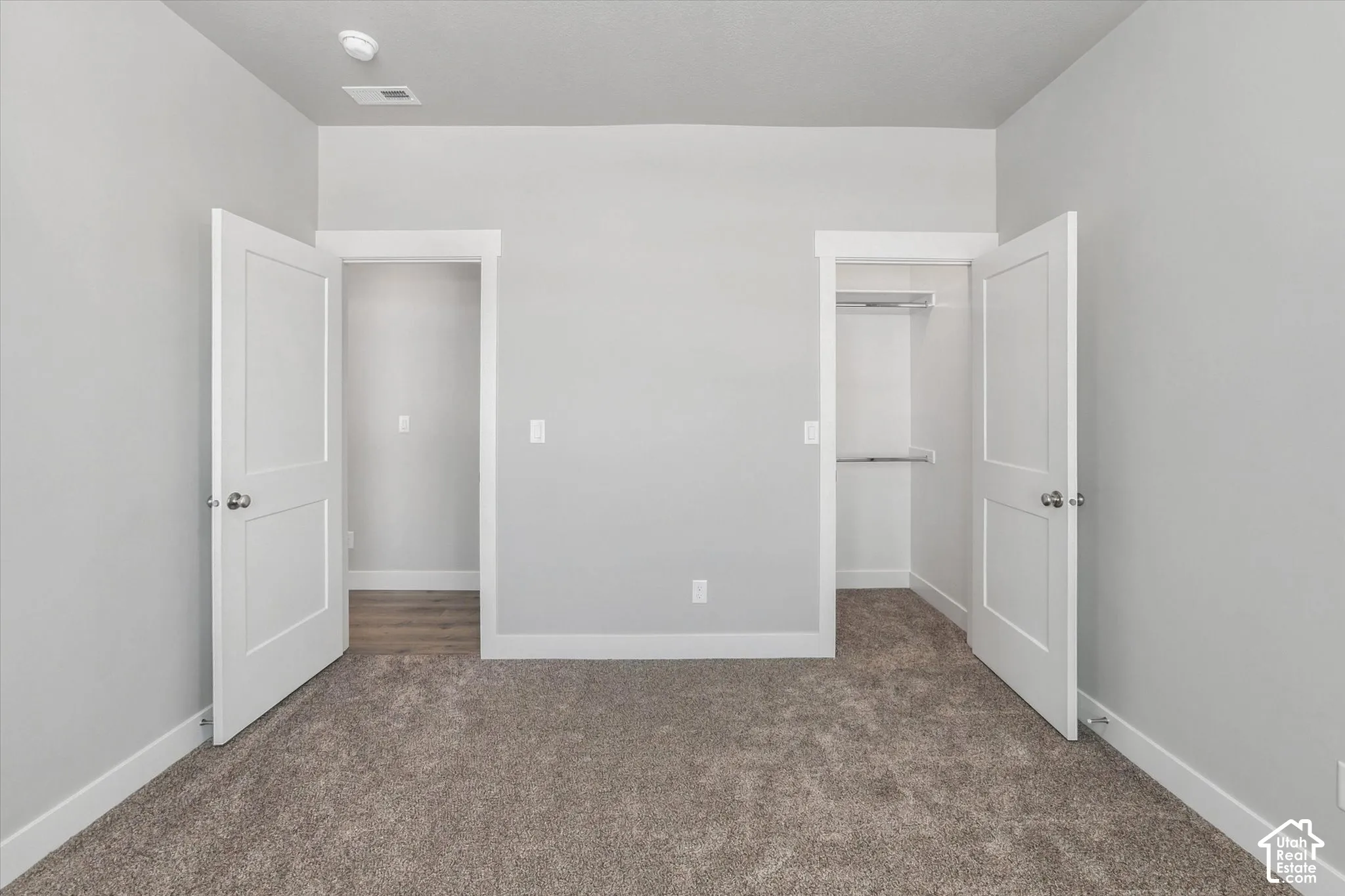 Plush carpet flooring, light gray wall paint, white trim, and a closet with a built-in shelf and hanging rod