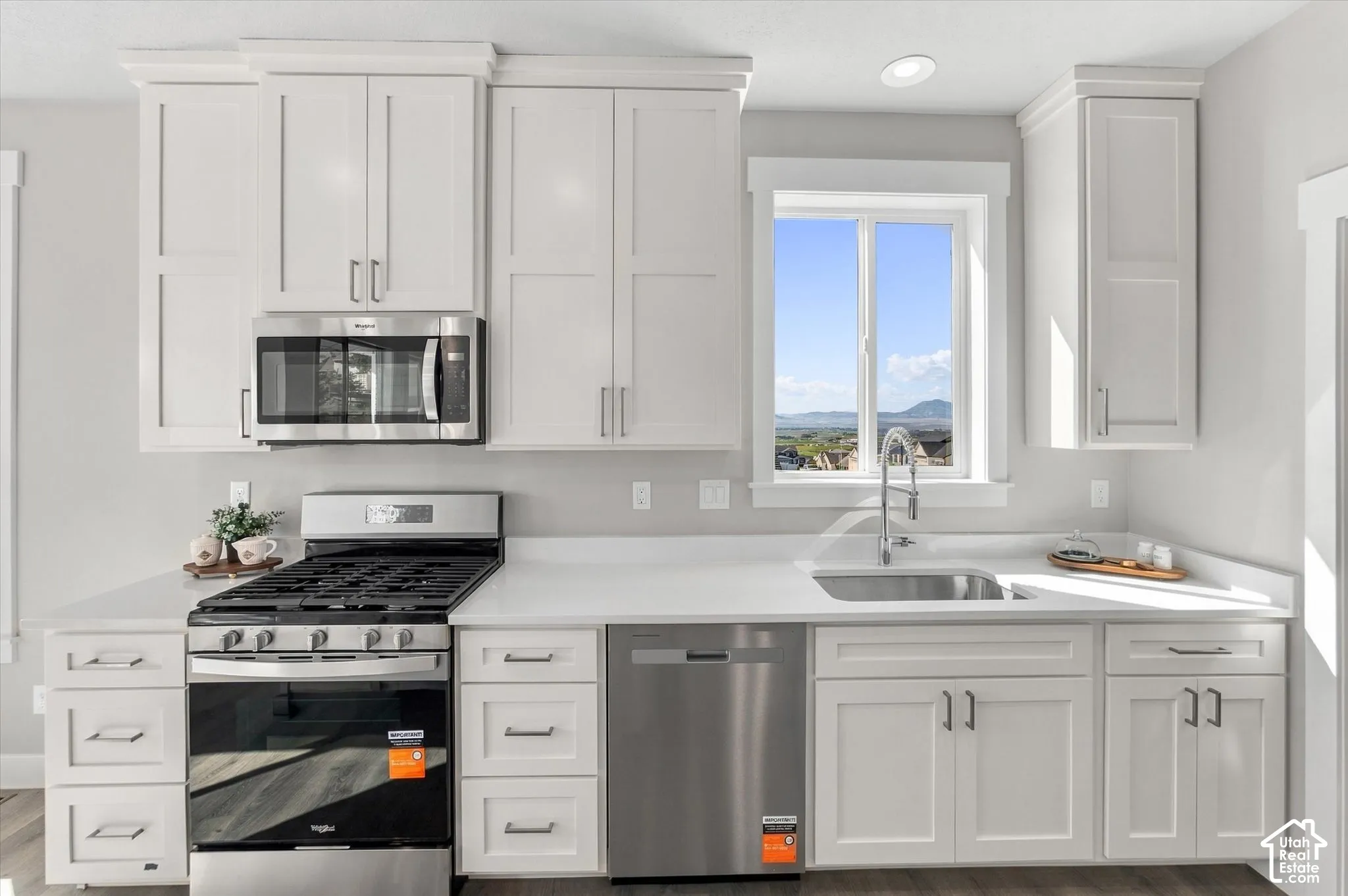 White shaker-style cabinetry, stainless steel appliances, light-toned countertops, undermount sink, and wood-finish flooring