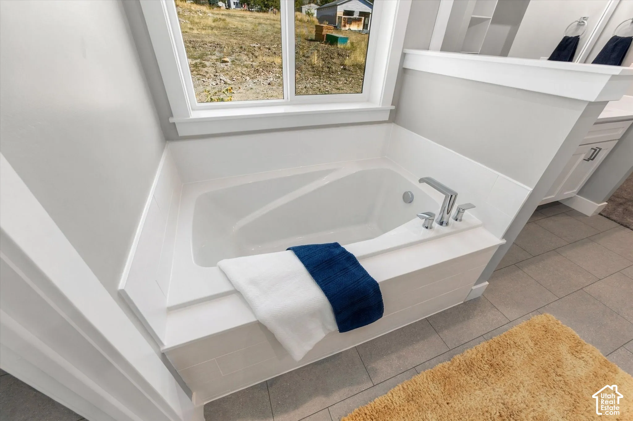 Built-in soaking tub with chrome fixtures, window with white trim, light gray wall paint, and light gray floor tile