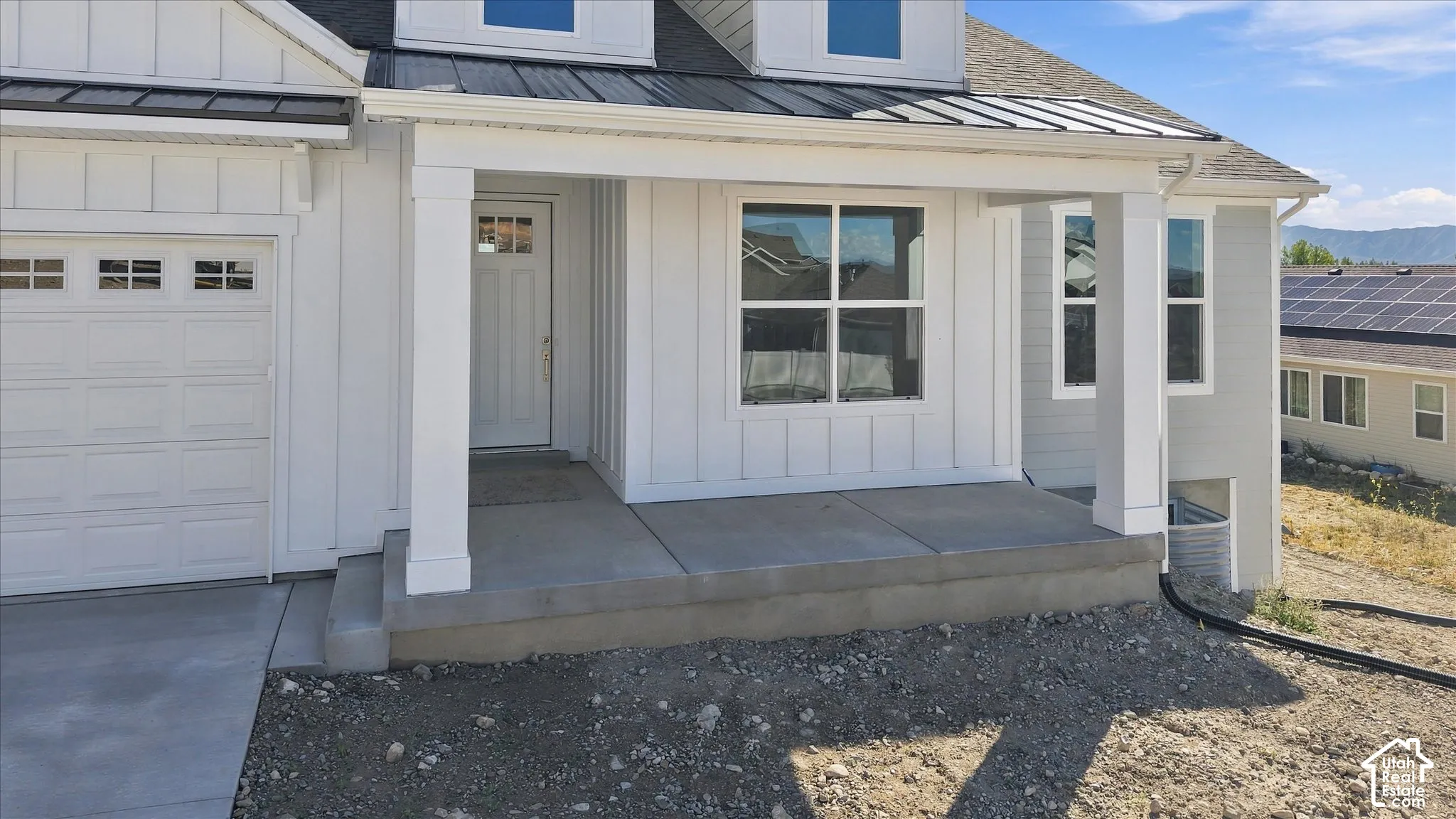 White board and batten siding, covered concrete porch, white paneled garage door, and a black metal awning