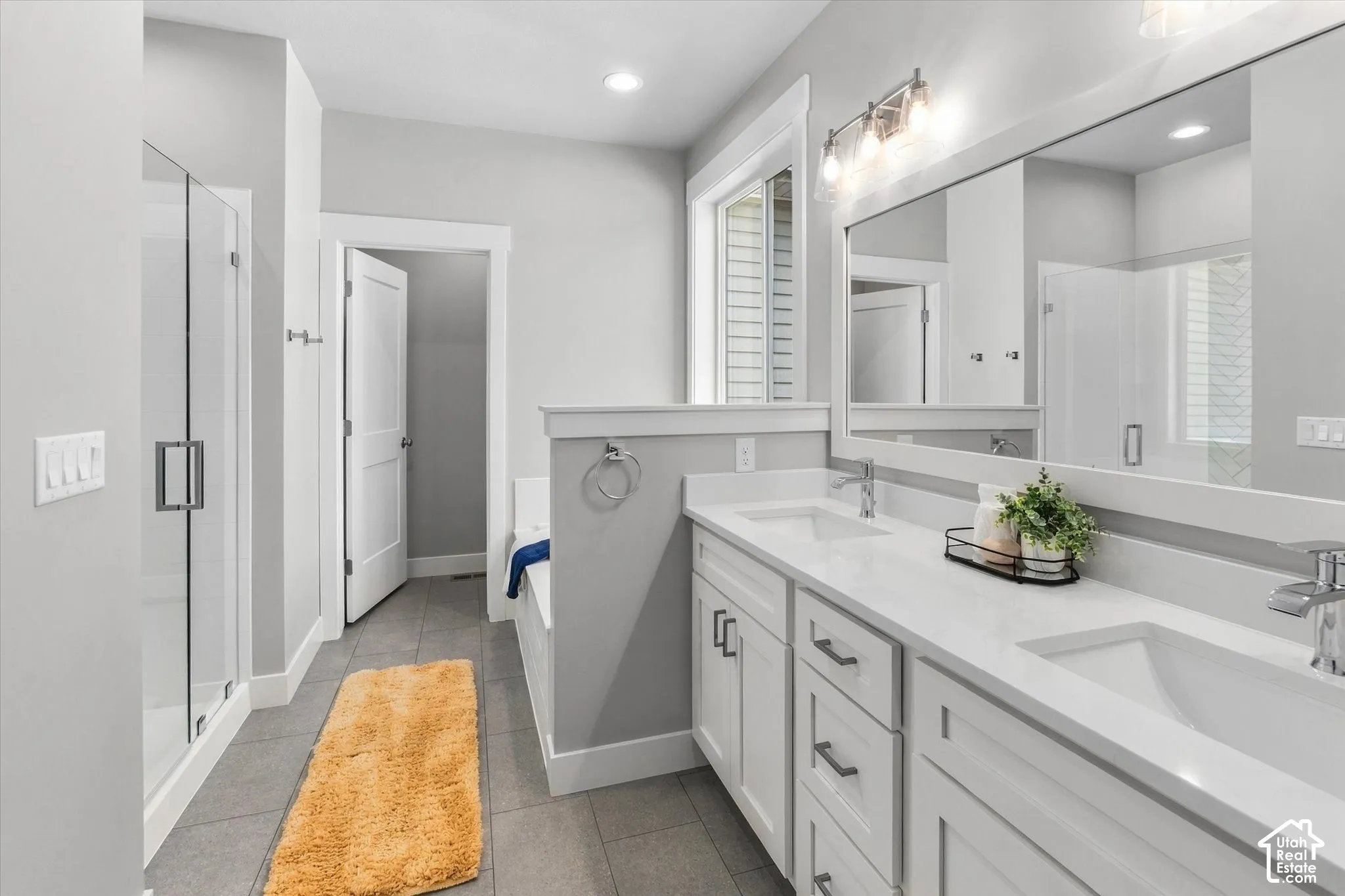 Dual vanity with white cabinetry and integrated sinks, a glass-enclosed shower, a built-in soaking tub, and tile flooring