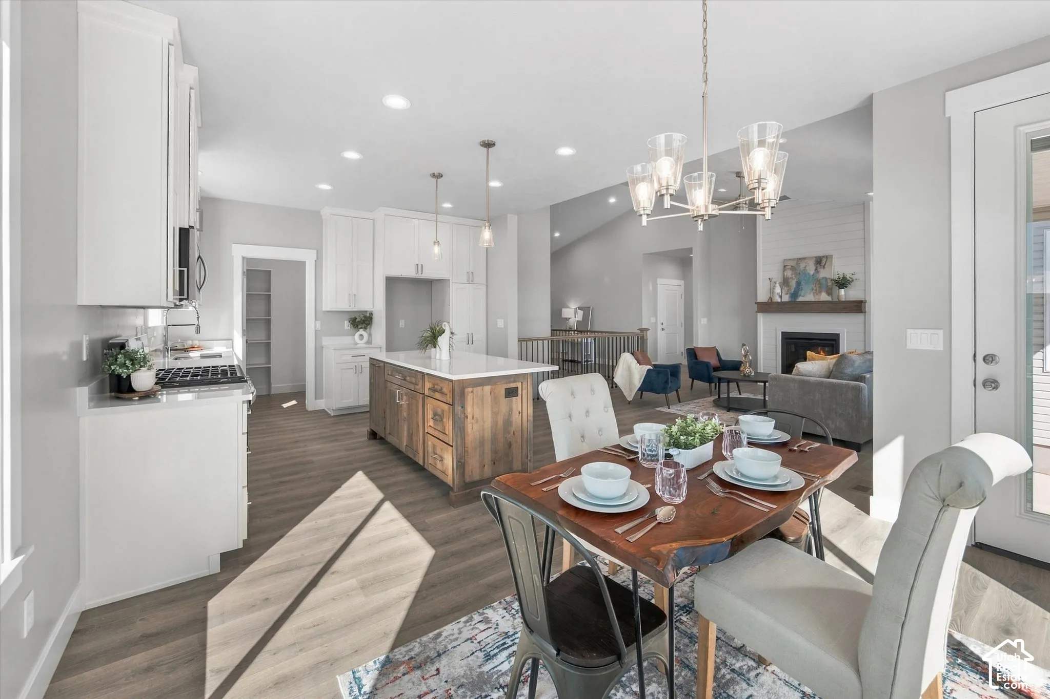 Open-concept living area with wood-finish flooring, a kitchen island with seating, white cabinetry, a built-in fireplace, and vaulted ceilings