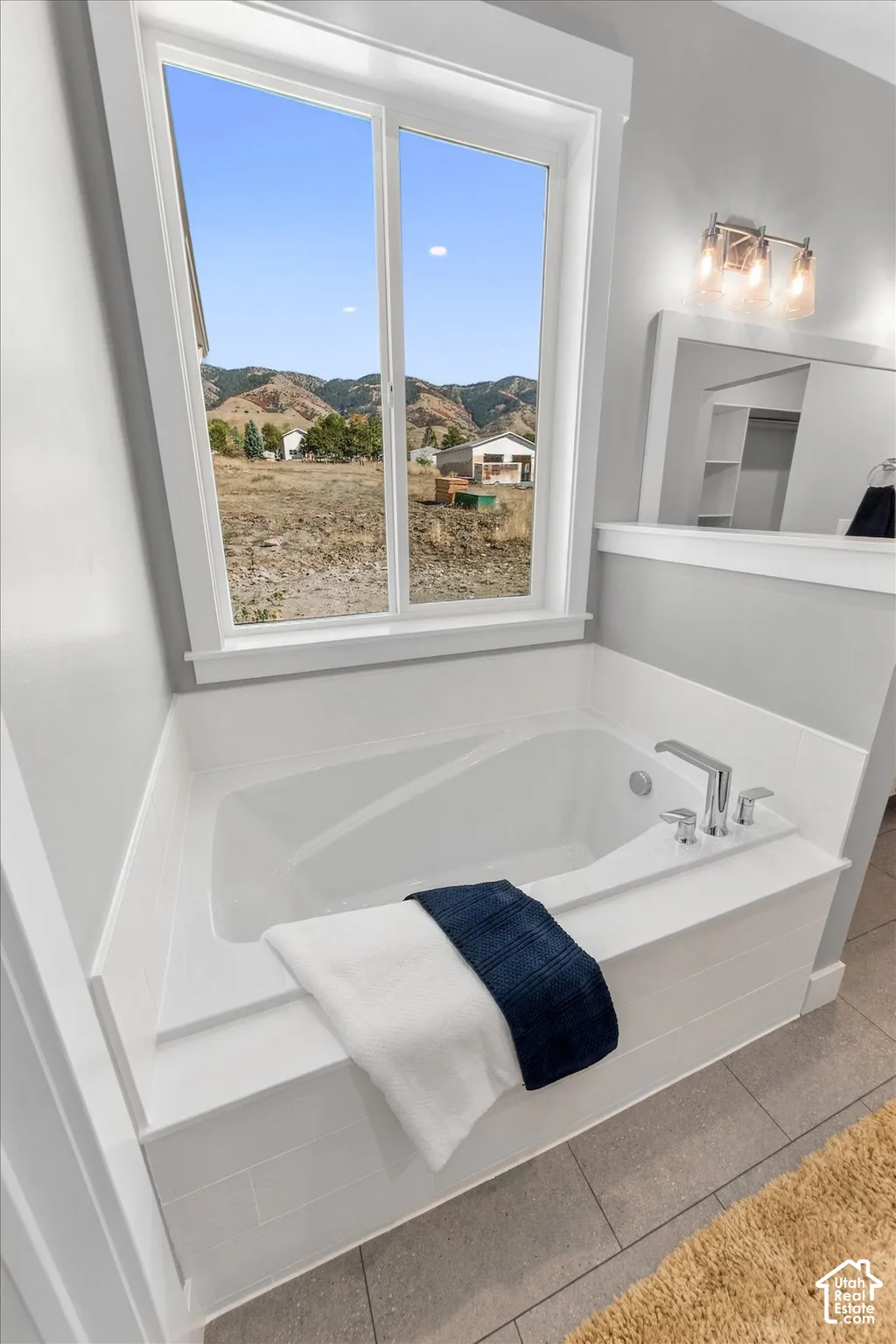 Built-in soaking tub with chrome fixtures, large window, brushed nickel light fixture, and tile flooring