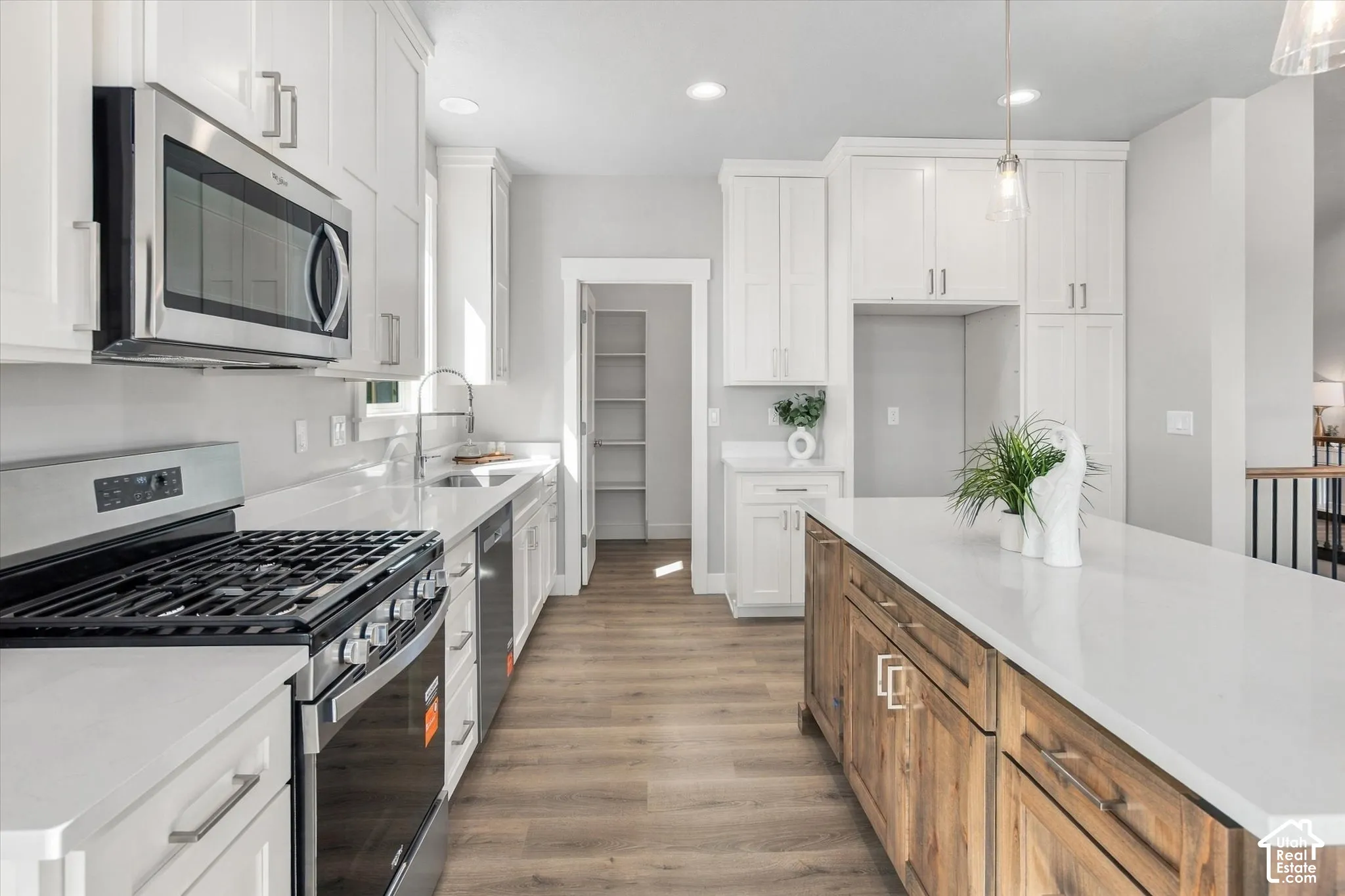 White cabinetry, stainless steel appliances, wood-finish flooring, central island with seating, and a walk-in pantry
