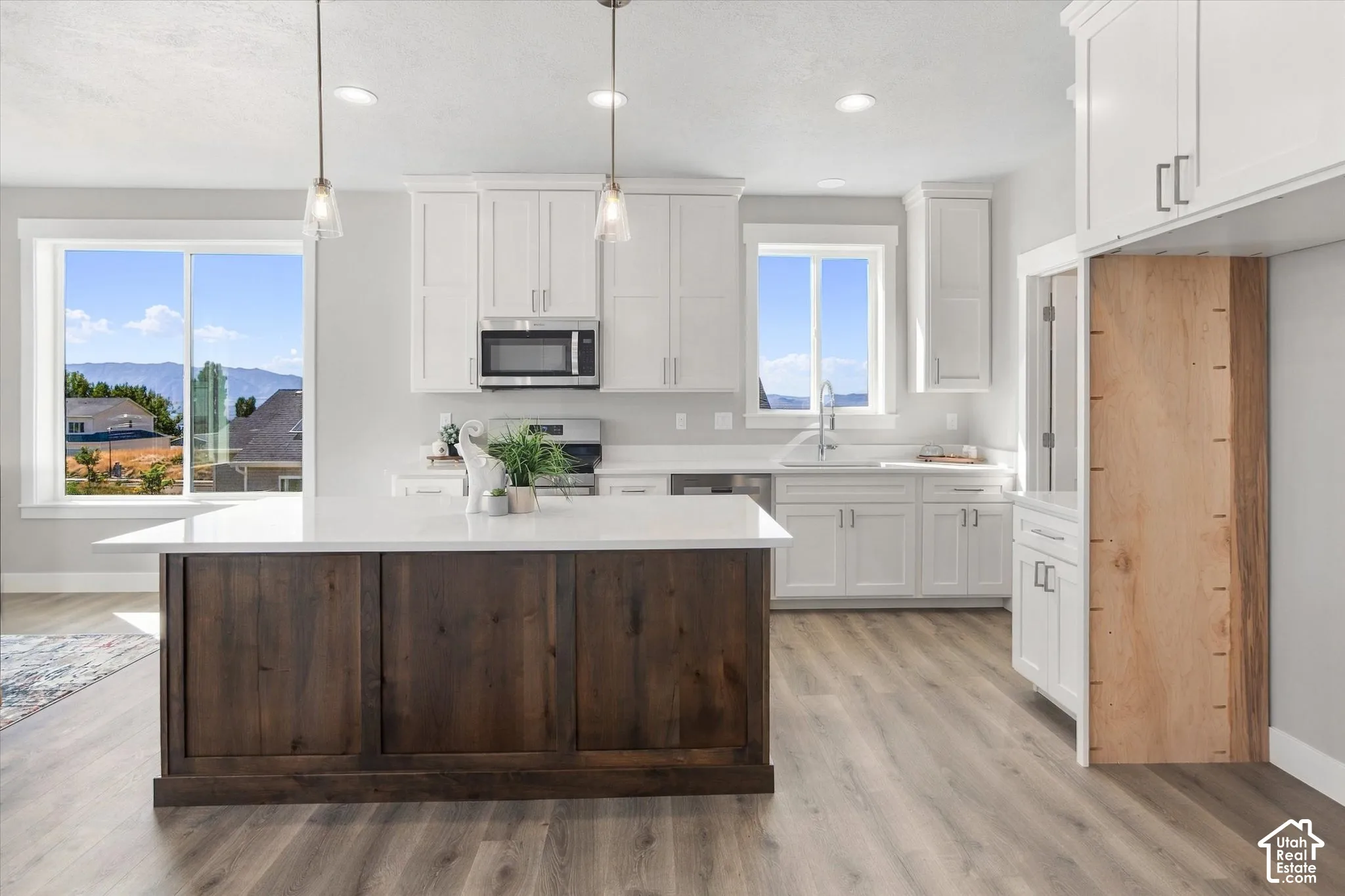 Kitchen featuring a dark wood-finish island with a white countertop, recessed lighting, pendant lights, and light wood-finish flooring