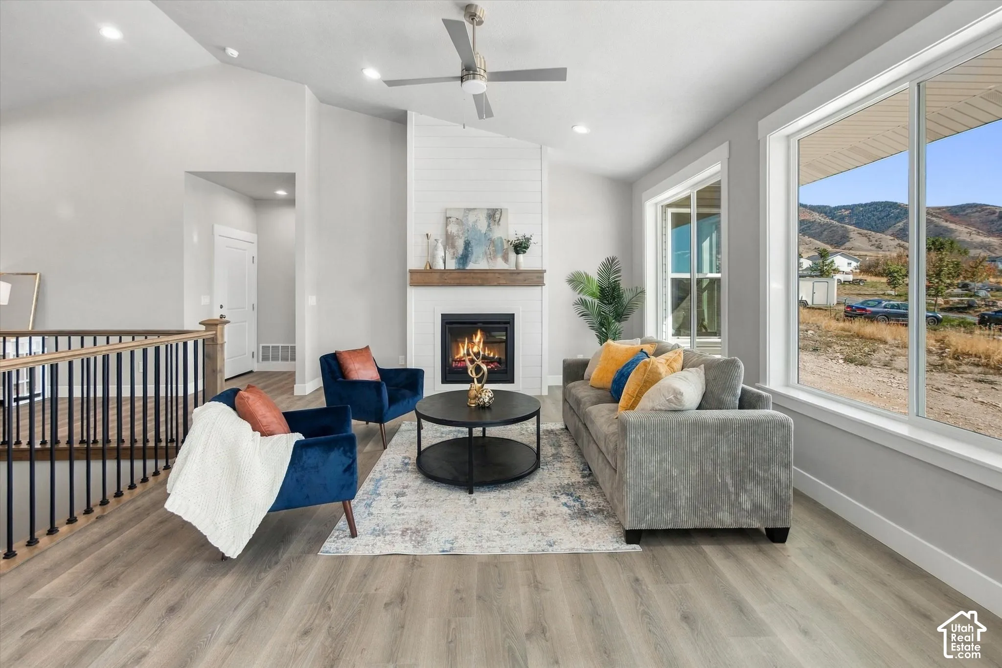 Vaulted ceiling with a ceiling fan, fireplace with a wood-finish mantel and shiplap surround, wood-finish flooring, and large windows