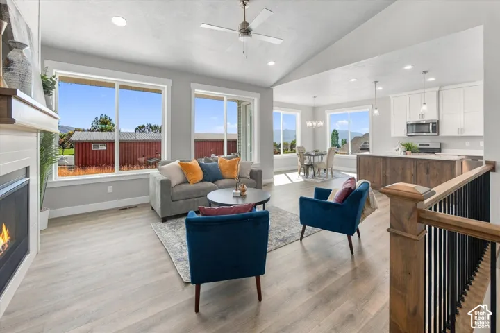 Open-concept living area with vaulted ceilings, wood-finish flooring, a built-in fireplace, and large windows