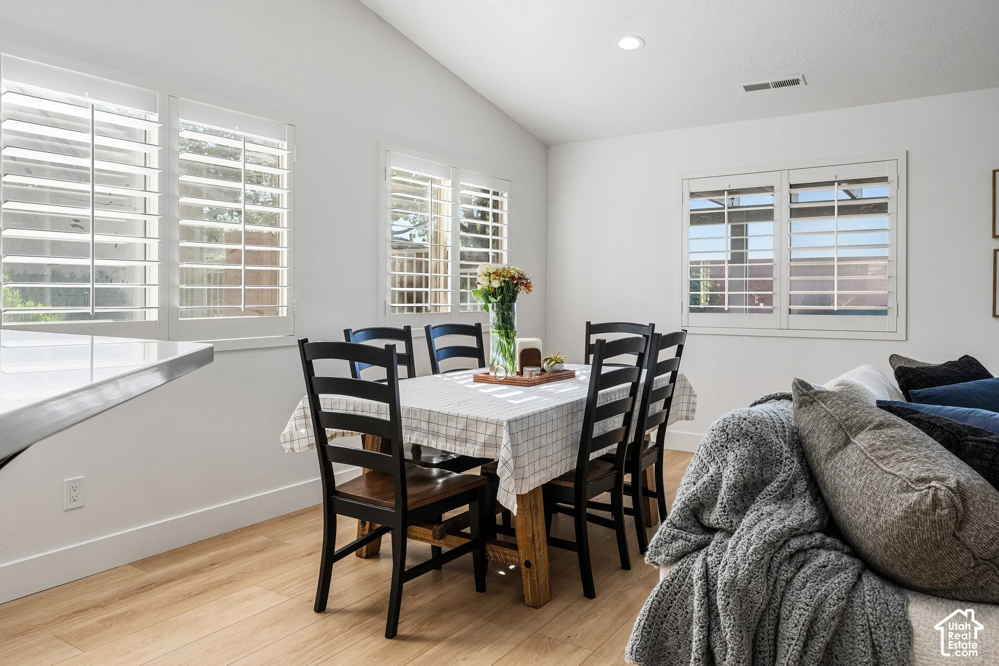 Vaulted ceiling with recessed lighting, wood-finish flooring, white plantation shutters, and a white countertop