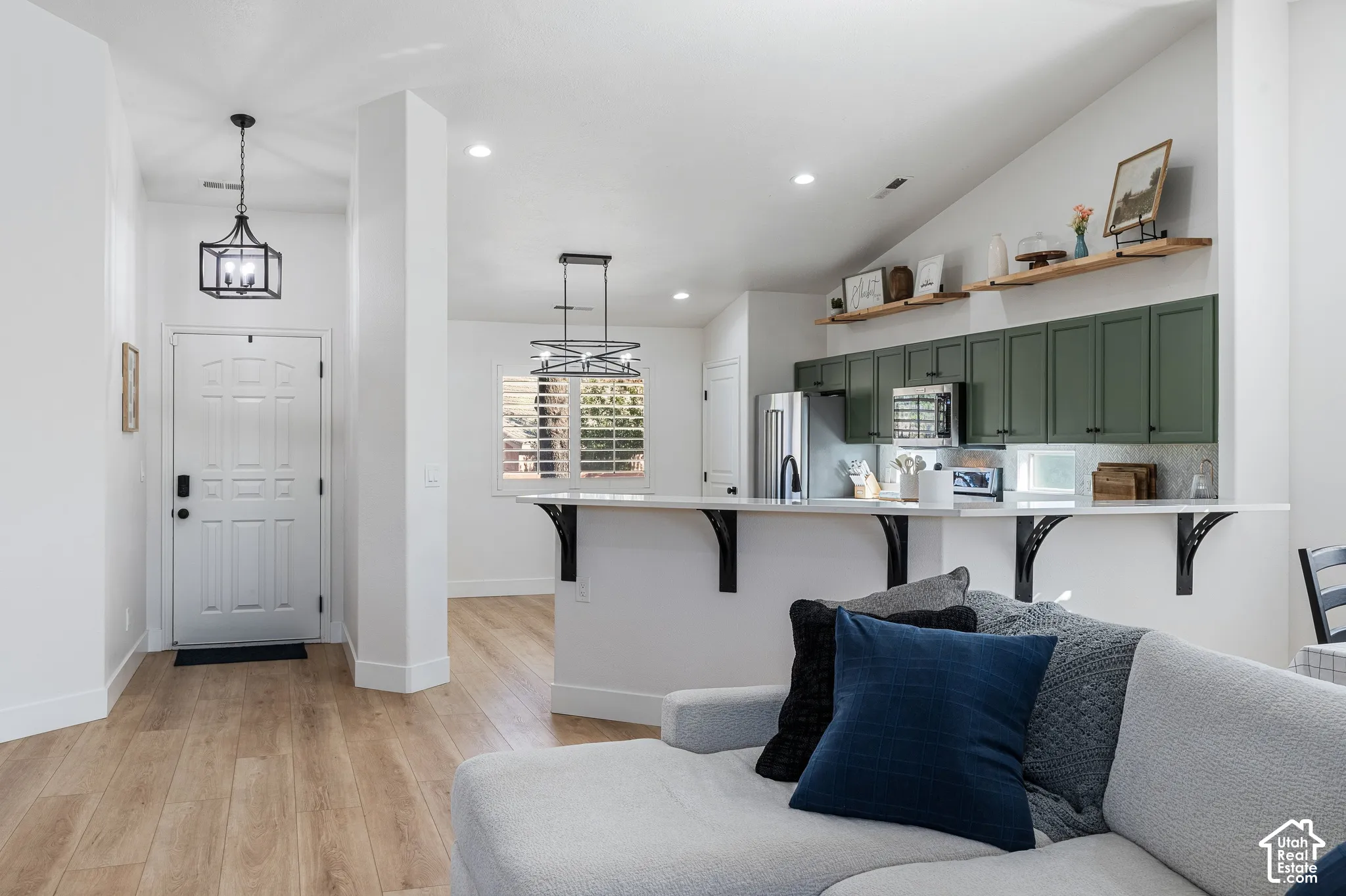 Vaulted ceilings, wood-finish flooring, white paneled entry door, kitchen with green cabinetry, and white countertops