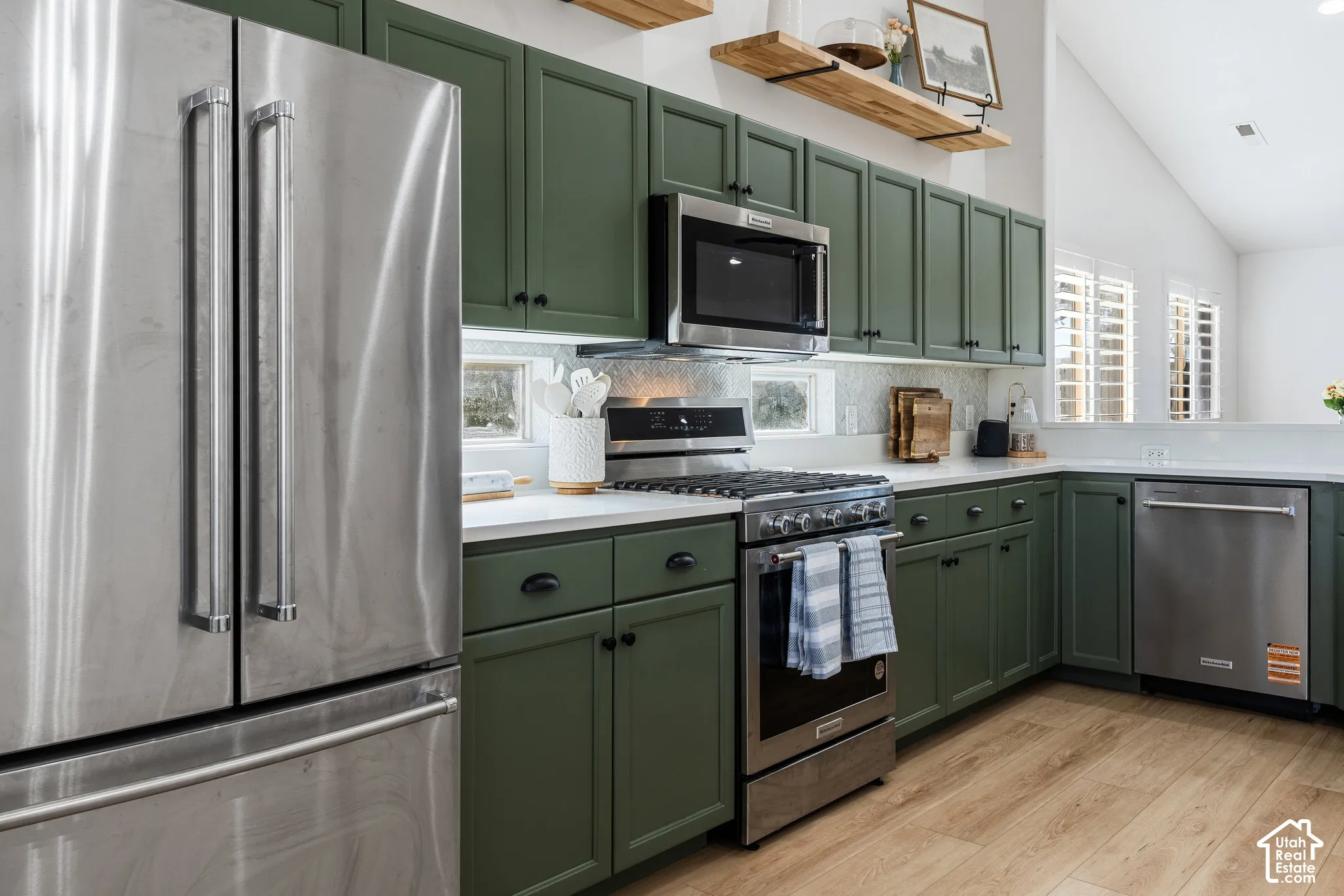 Kitchen featuring green cabinetry, stainless steel appliances, white countertops, wood-finish flooring, and open shelving
