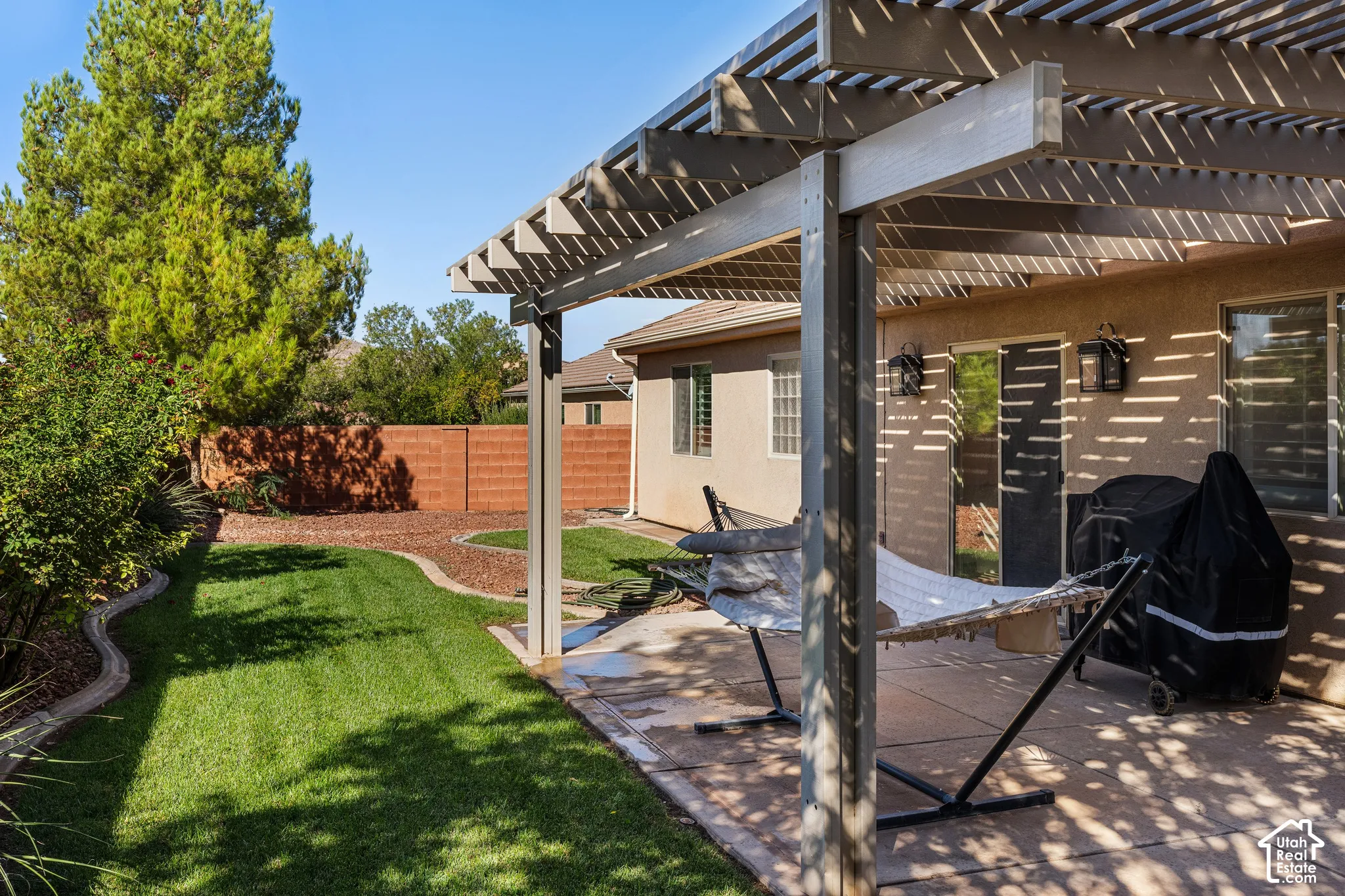 Backyard featuring a slatted pergola, concrete patio, and a manicured lawn