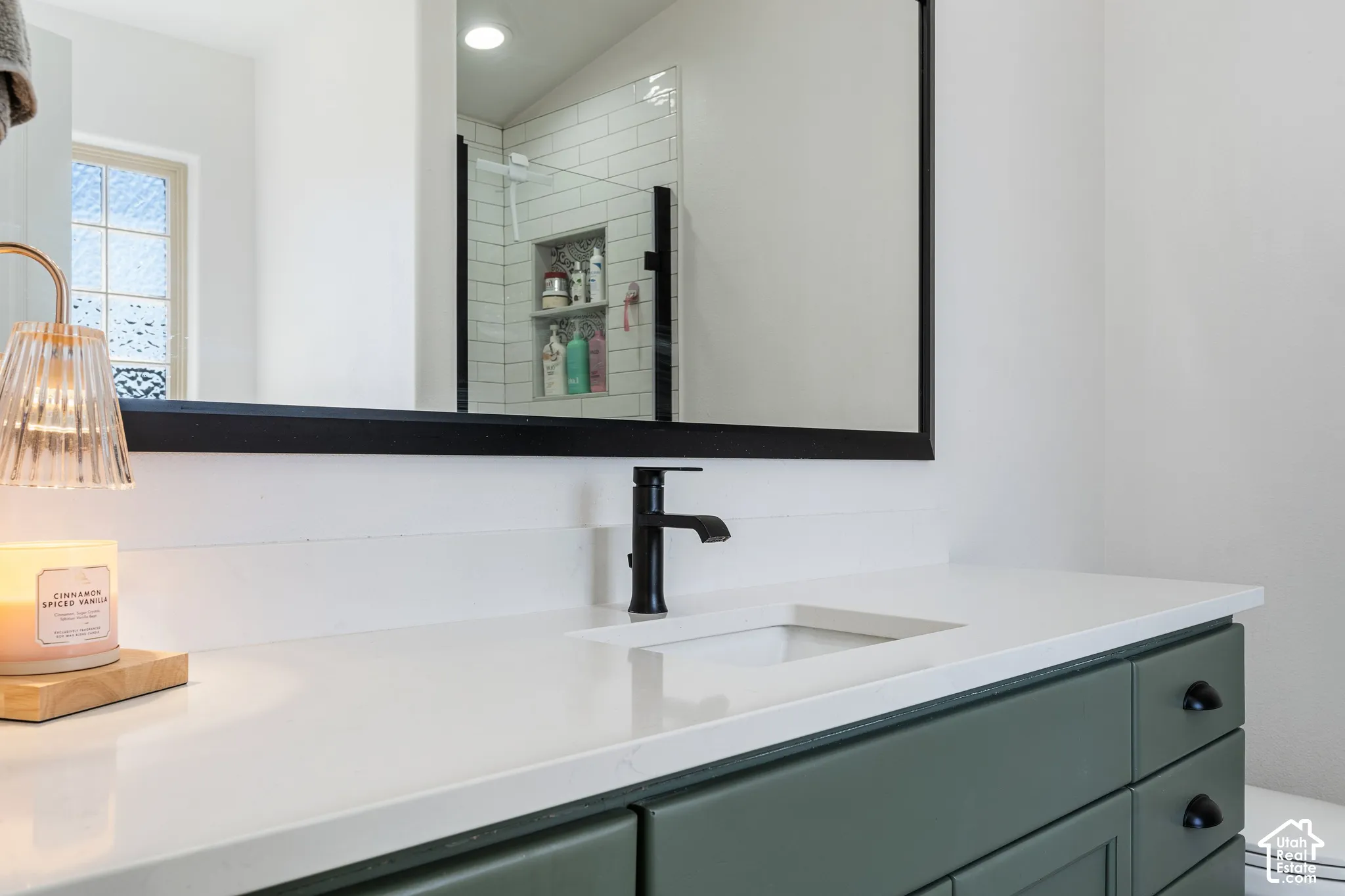 White countertop with an integrated rectangular sink, matte black faucet, and green cabinetry