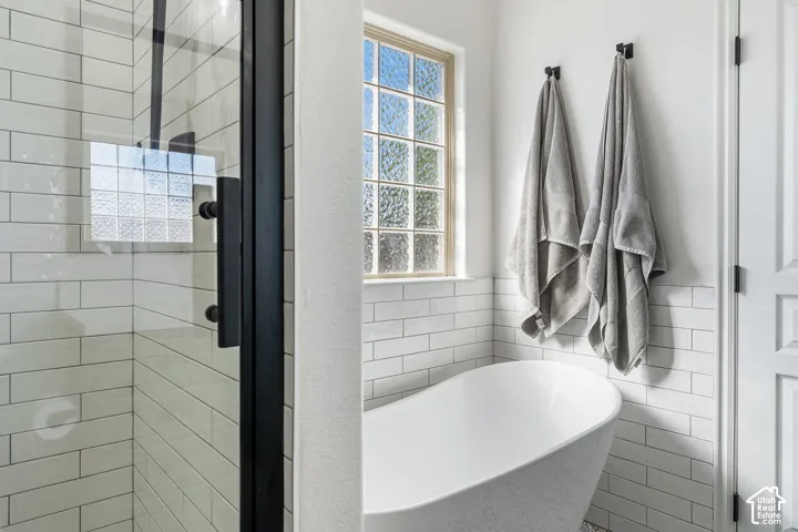 Freestanding soaking tub, white subway tile surround, textured glass window, and a shower with a black-framed glass enclosure