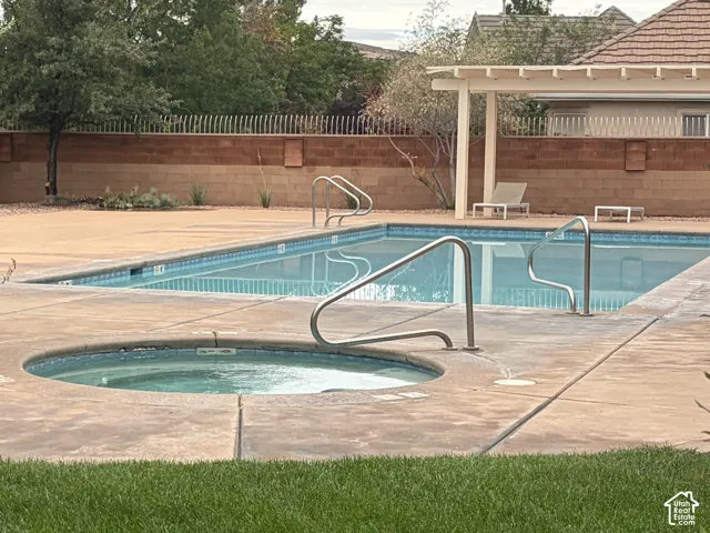 Integrated spa and pool with concrete decking, perimeter wall, and a shaded pergola
