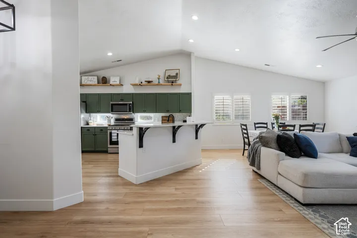Vaulted ceilings, wood-finish flooring, recessed lighting, kitchen island with countertop seating, and green cabinetry