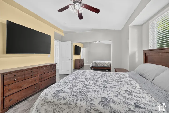 Vaulted ceiling with a ceiling fan, wood-finish flooring, and natural light from a window with blinds