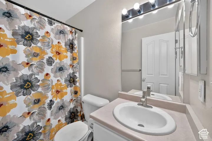 Bathroom featuring a vanity with an integrated sink, a large mirror with overhead lighting, and a commode
