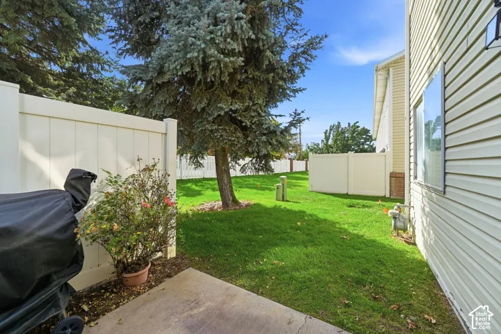 Concrete patio with a manicured lawn, established privacy fencing, and mature trees