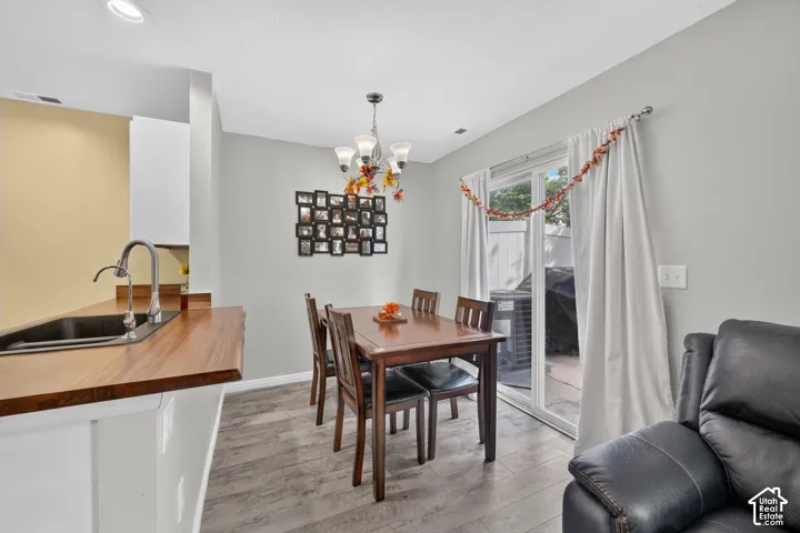 Wood-finish flooring, kitchen pass-through with wood-finish countertop, stainless steel sink with gooseneck faucet, overhead chandelier, and sliding glass door