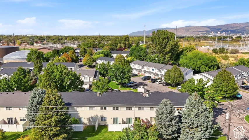 Townhome community featuring multiple units with individual patios, surrounded by mature trees, and mountainous terrain in the distance
