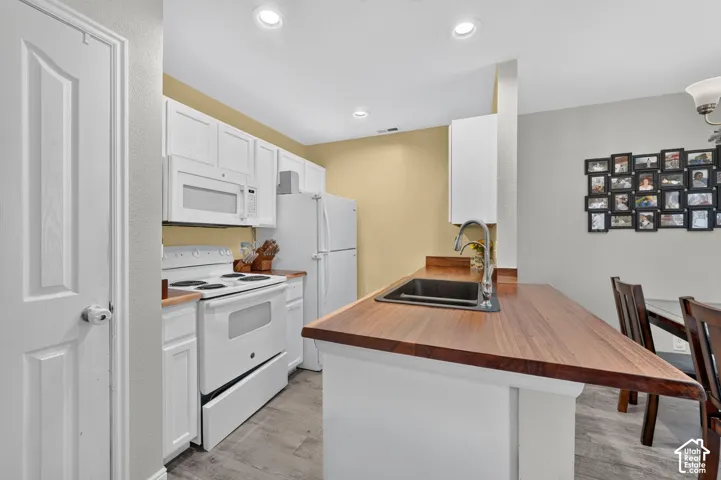 Kitchen with white cabinetry, wood-finish countertops, and an undermount sink