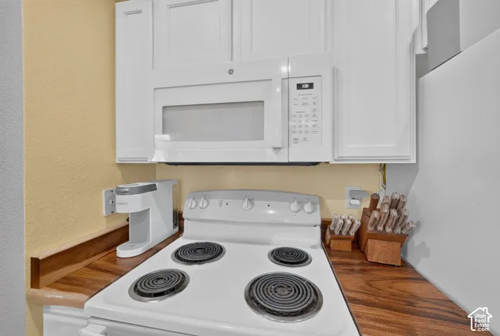 White cabinetry with panel doors, integrated over-the-range microwave, white electric range, and wood-finish countertops