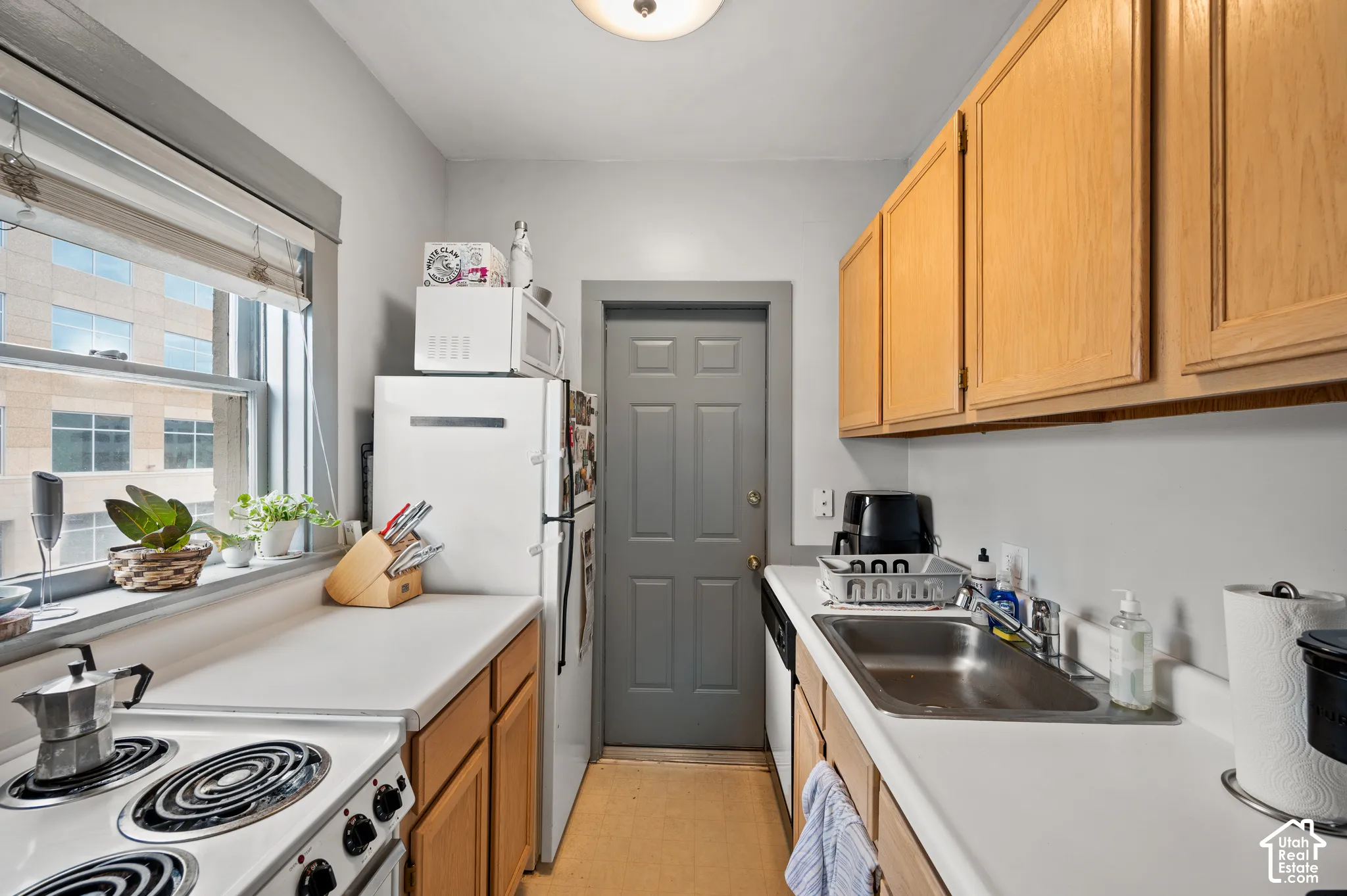 Galley kitchen with wood-finish cabinetry, white countertops, stainless steel sink, and window with natural light
