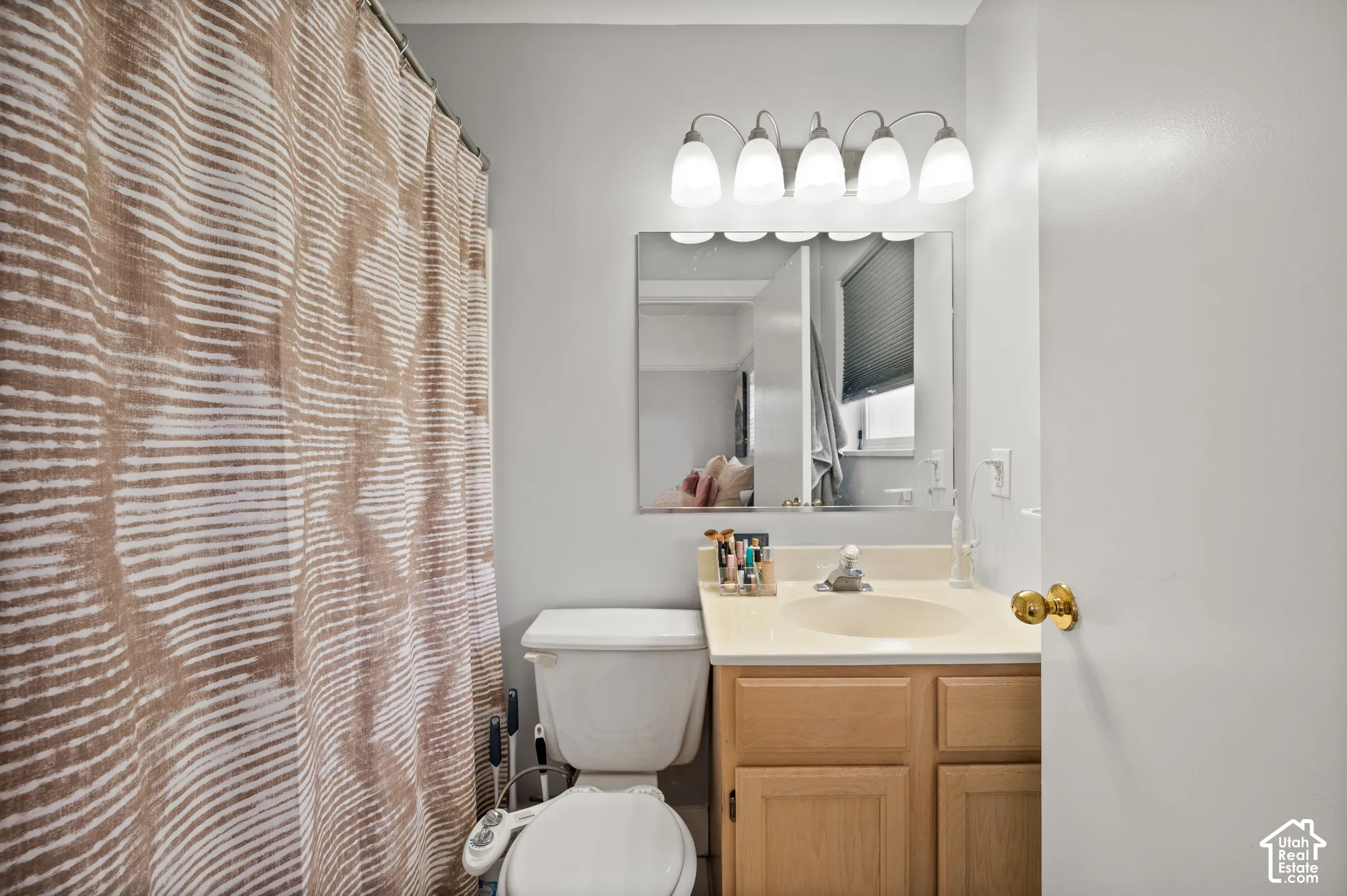 Bathroom featuring a single vanity with a laminate countertop, light wood-finish cabinetry, an undermount sink, and a framed mirror